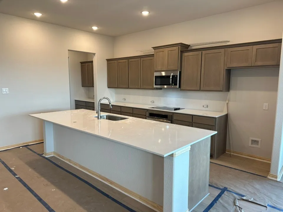 Kitchen featuring a large island with white countertop, stainless steel appliances, wood-finish cabinetry, and recessed lighting
