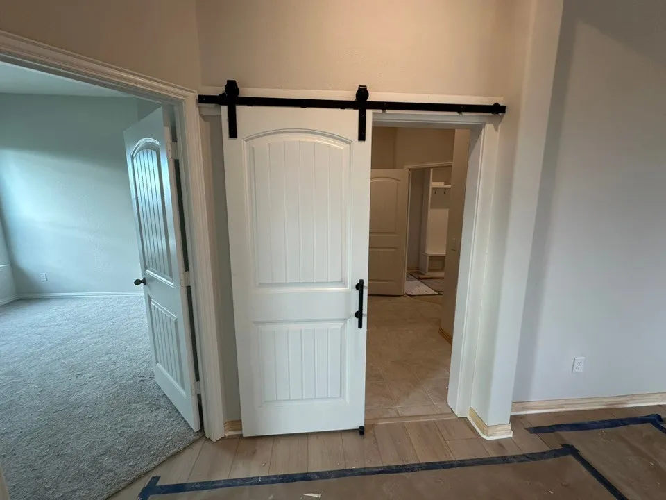 White paneled barn door with matte black hardware, wood-finish flooring, light grey wall paint, and white trim