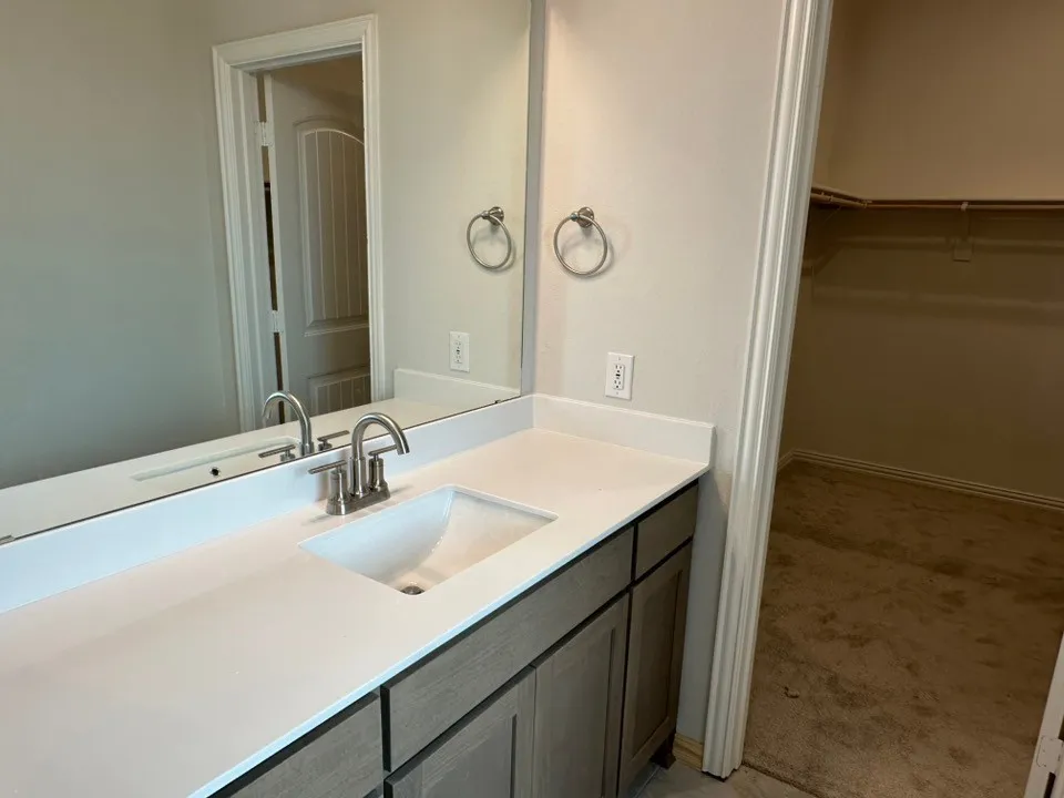 Vanity with a white countertop and integrated sink, brushed nickel faucet, large wall mirror, and wood-finish cabinetry