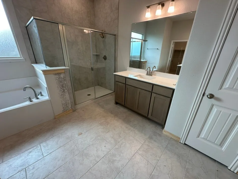 Alcove bathtub with deck-mounted faucet, walk-in shower with glass enclosure, single vanity with integrated sink, rectangular mirror, and tile flooring