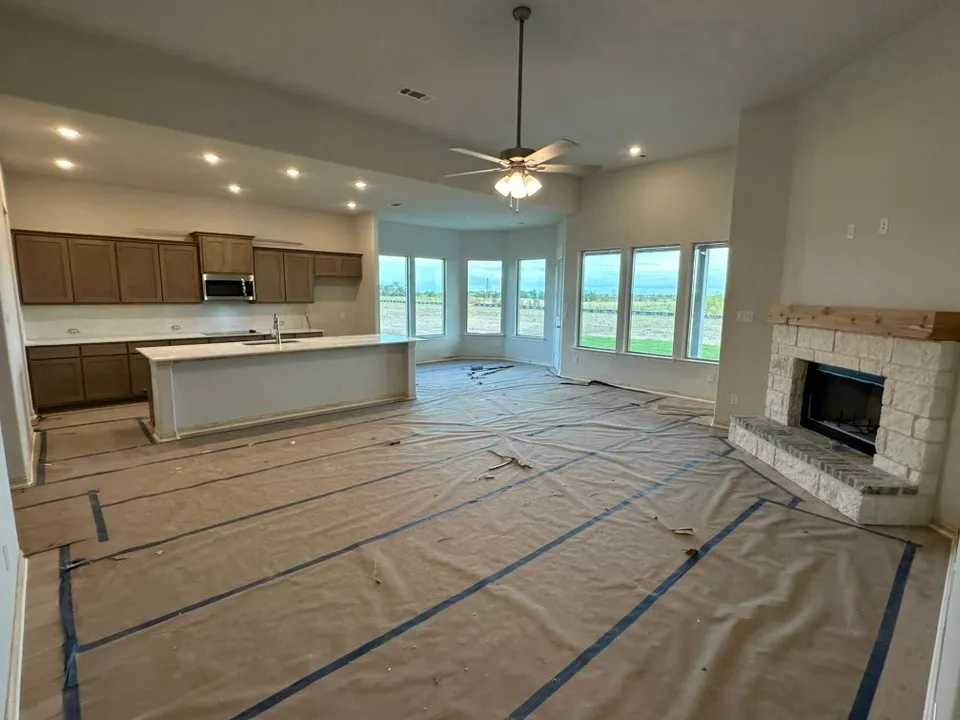 Open-concept living space with a kitchen island, integrated stainless steel microwave, stone fireplace with wood mantel, a ceiling fan, and multiple windows