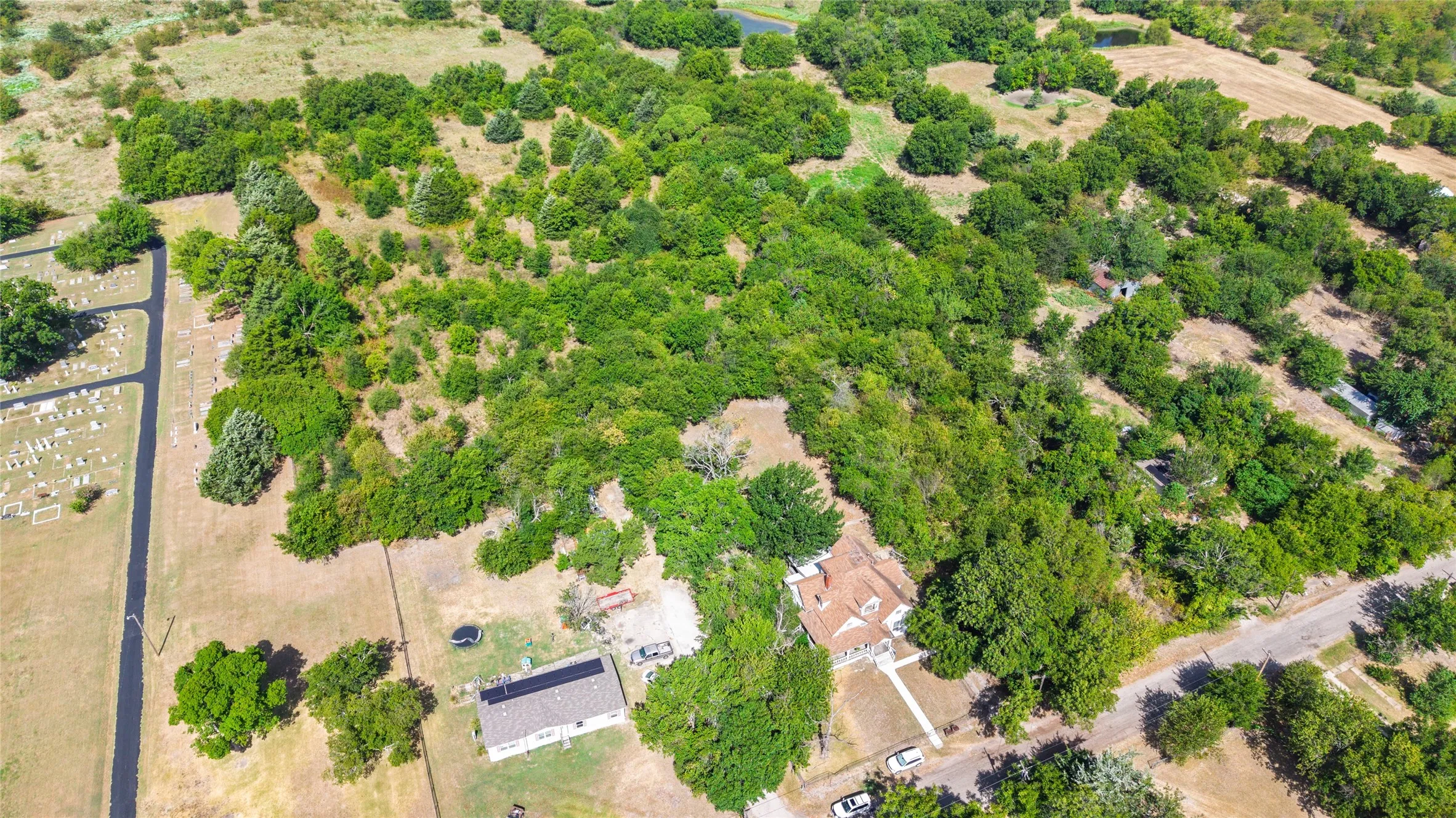 Extensive acreage featuring diverse tree coverage, a residential structure with a light-colored roof, and a separate structure with solar panels