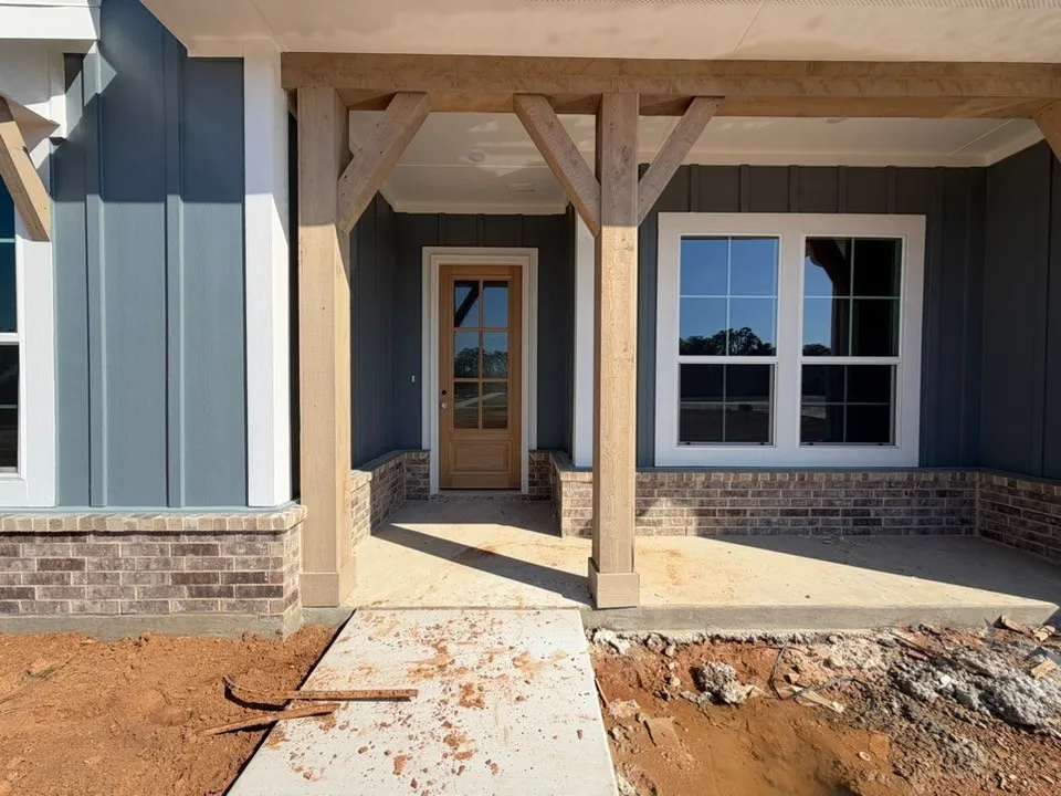 Front entry featuring a wood-panel door with glass inserts, board and batten siding, brick foundation, and substantial wood porch columns
