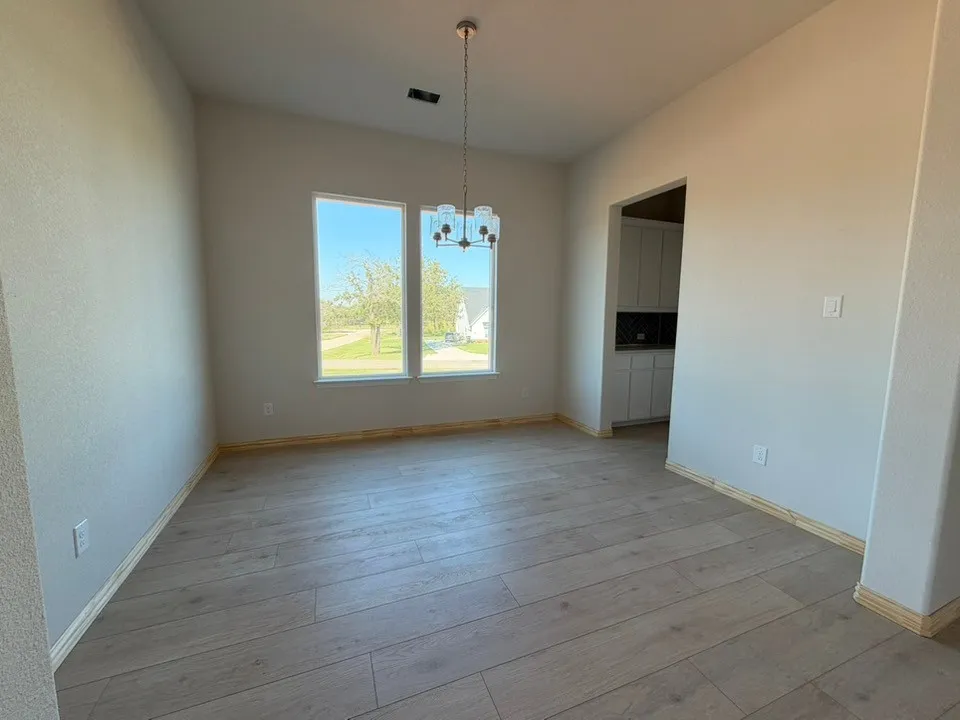 Spacious room featuring wood-finish flooring, two large windows, and a hanging chandelier