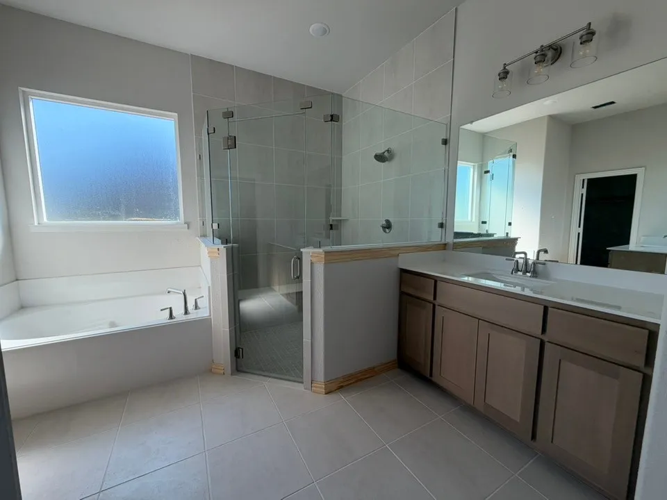 Spacious bathroom featuring a built-in bathtub, a walk-in shower with clear glass enclosure, a vanity with dual sinks, and a large mirror with integrated lighting