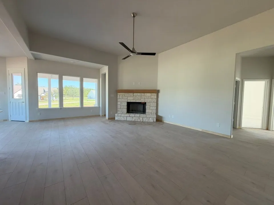 Vaulted ceilings with a ceiling fan, wood-finish flooring, stone-clad fireplace with wood mantel, and multiple windows