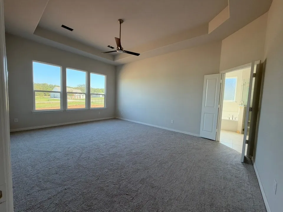 Tray ceiling with recessed lighting, three large windows, textured carpeting, ceiling fan with wood-finish blades, and double panel interior doors