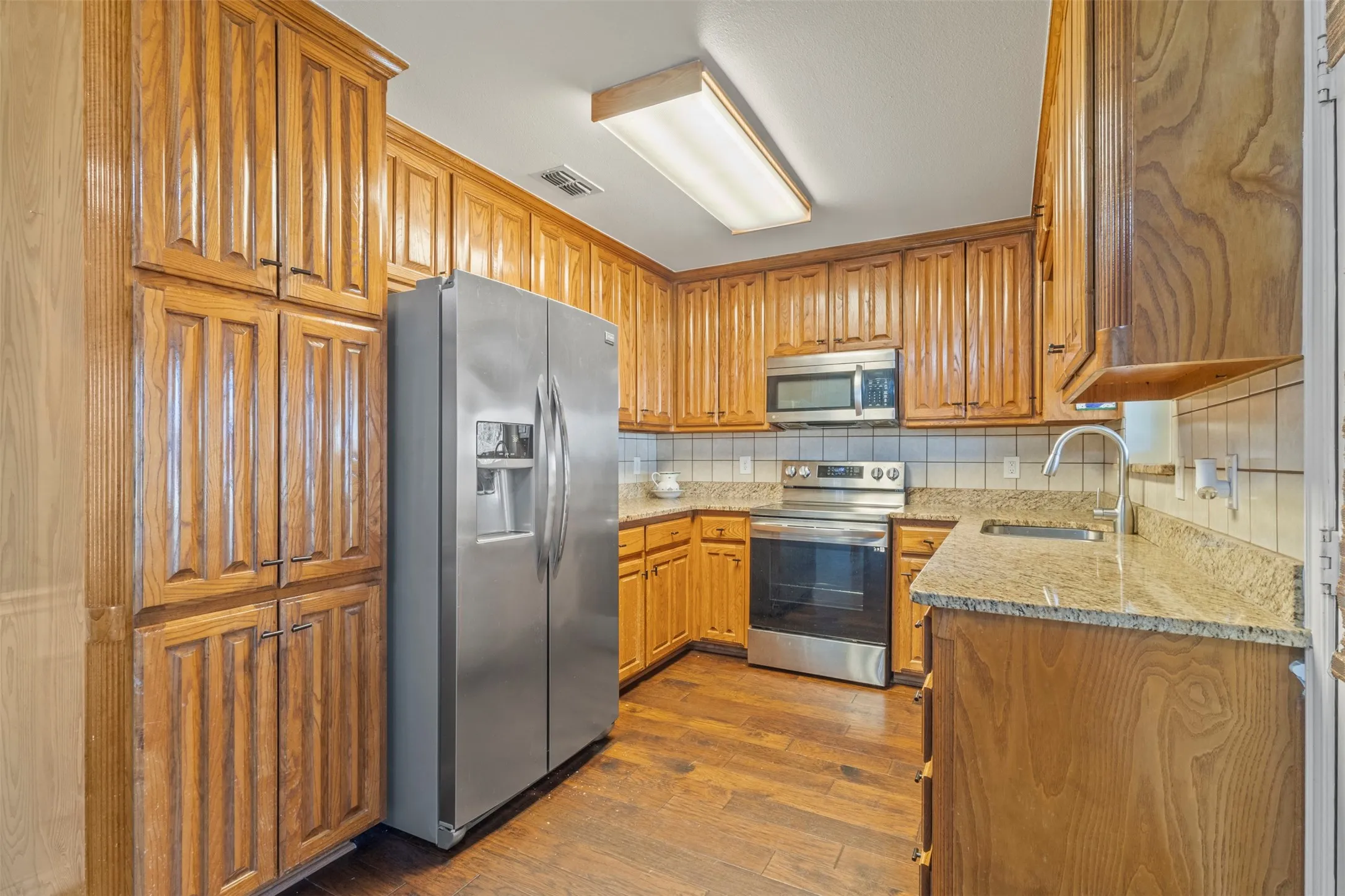 Wood-finish flooring, ample wood cabinetry, stainless steel appliances, and stone countertops