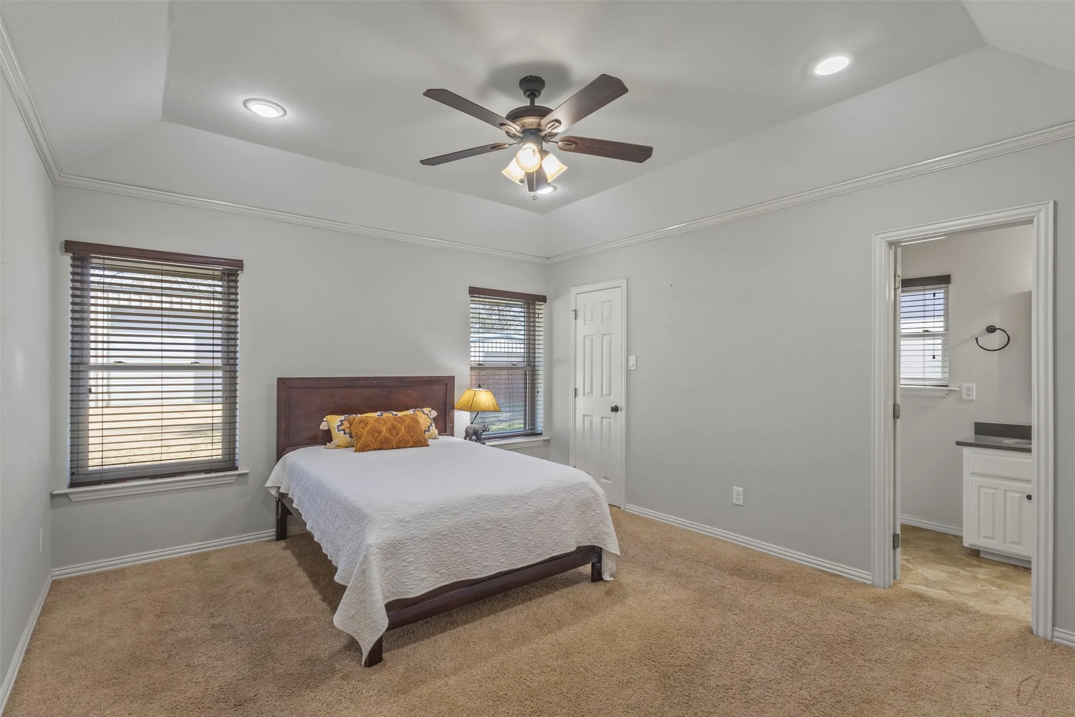 Spacious primary bedroom showcasing warm wood-finish flooring, recessed ceiling lighting, and a ceiling fan with integrated light fixture