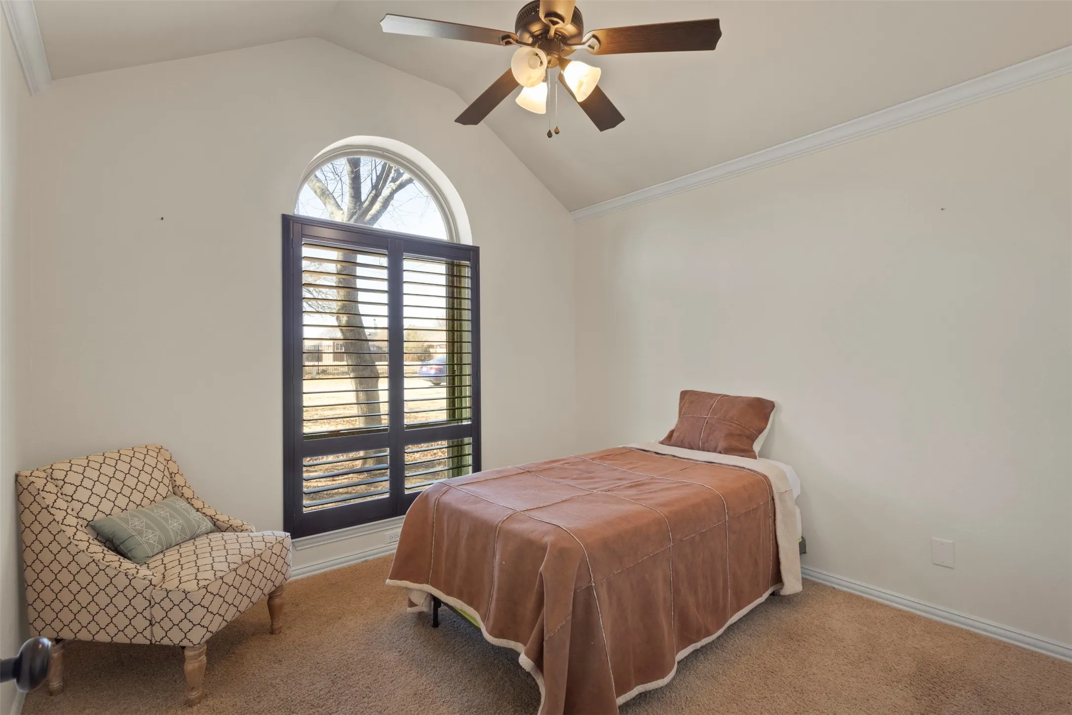 Vaulted ceiling with crown molding, arched window, plantation shutters, and ceiling fan