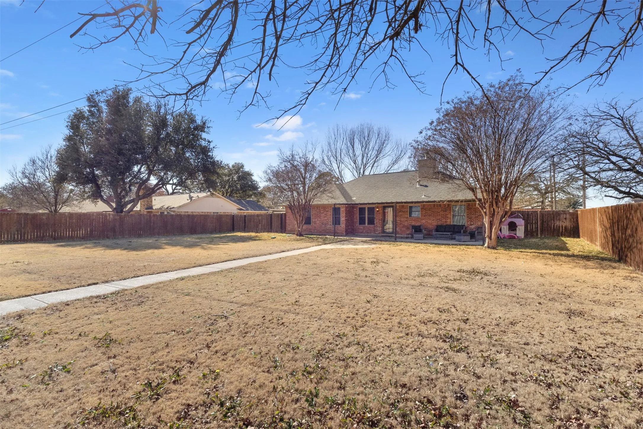 Expansive backyard featuring a concrete pathway, privacy fencing, and mature trees