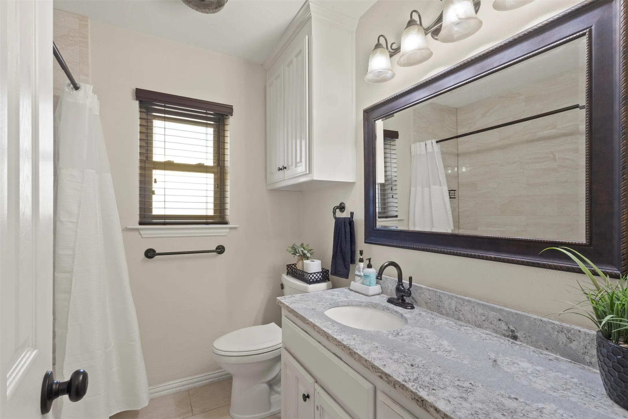 Vanity with a single basin, a rectangular framed mirror, and a three-light fixture