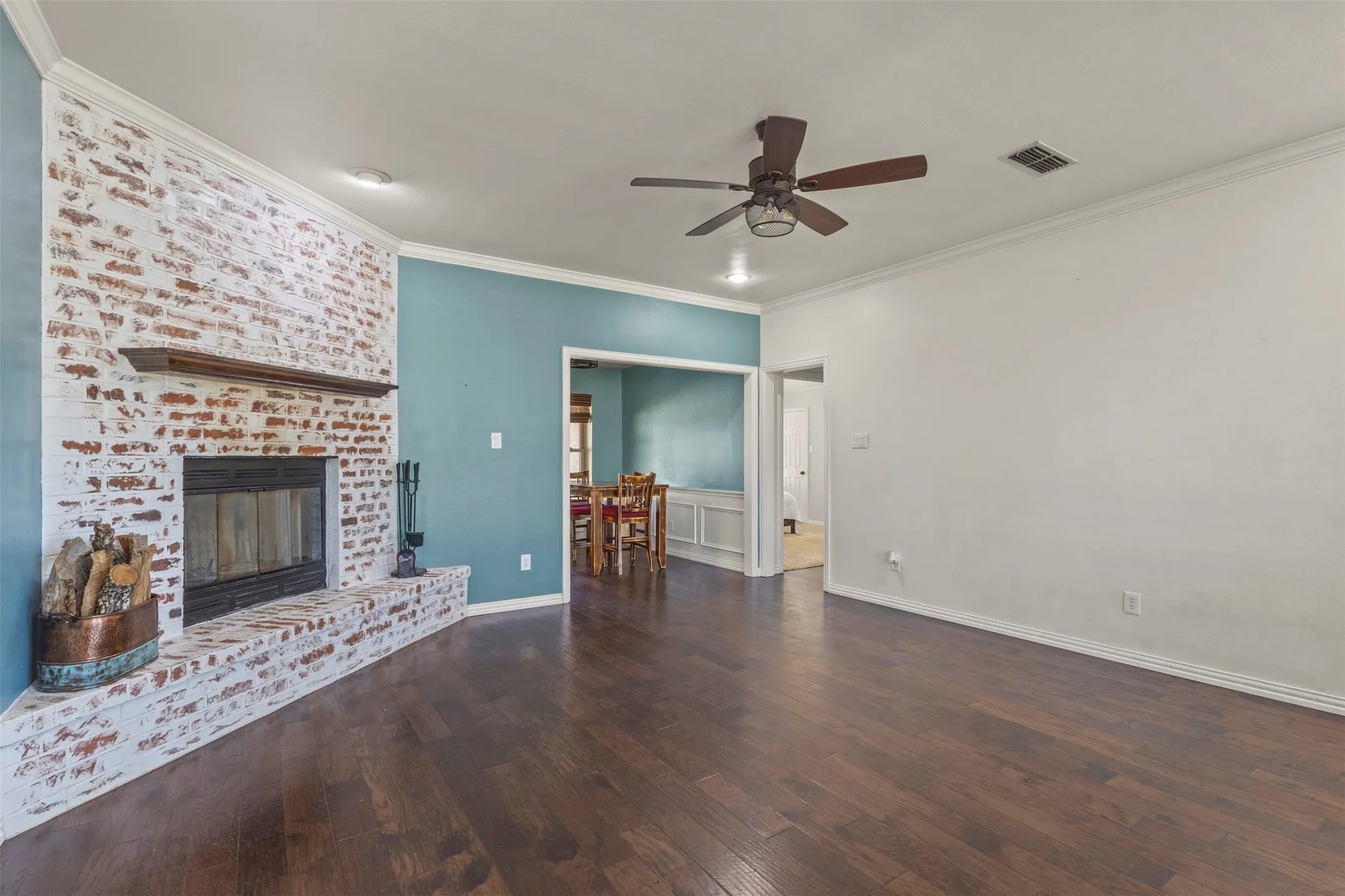 Fireplace with whitewashed brick surround, wood-finish flooring, ceiling fan, and crown molding
