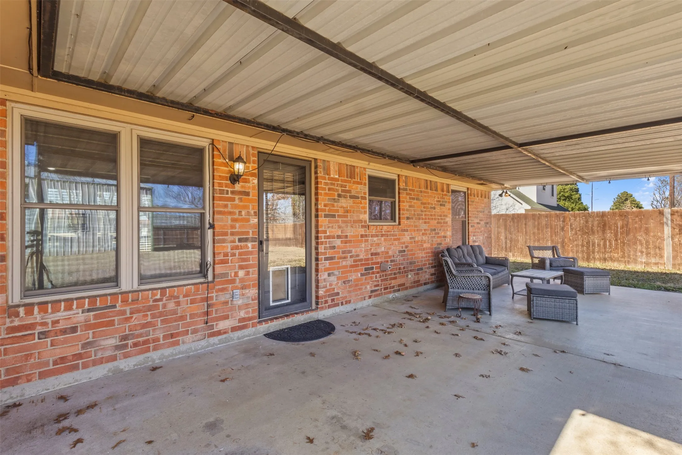 Covered concrete patio with brick exterior and fenced yard