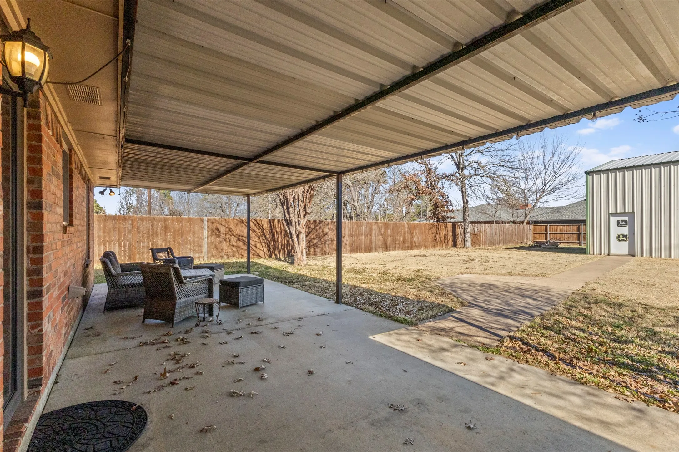 Covered concrete patio with a permanent metal roof structure, brick exterior, and a fenced backyard