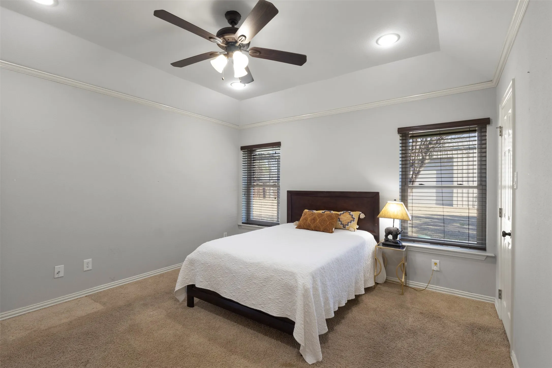 Tray ceiling with recessed lighting, crown molding, two windows with wood-finish blinds, and a ceiling fan