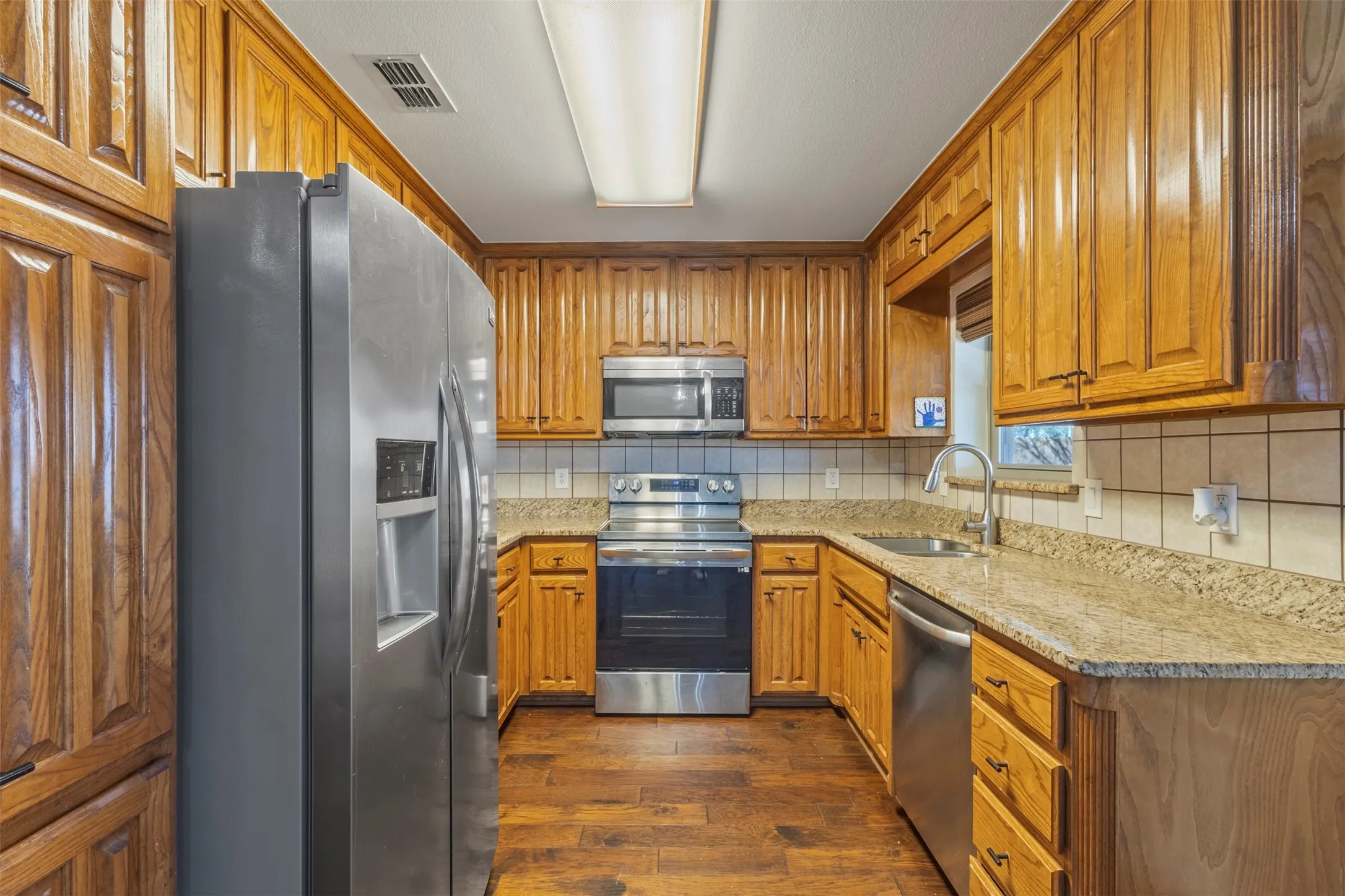 Wood-finish flooring, full height wood cabinetry, stainless steel appliances, stone countertops, and a tile backsplash