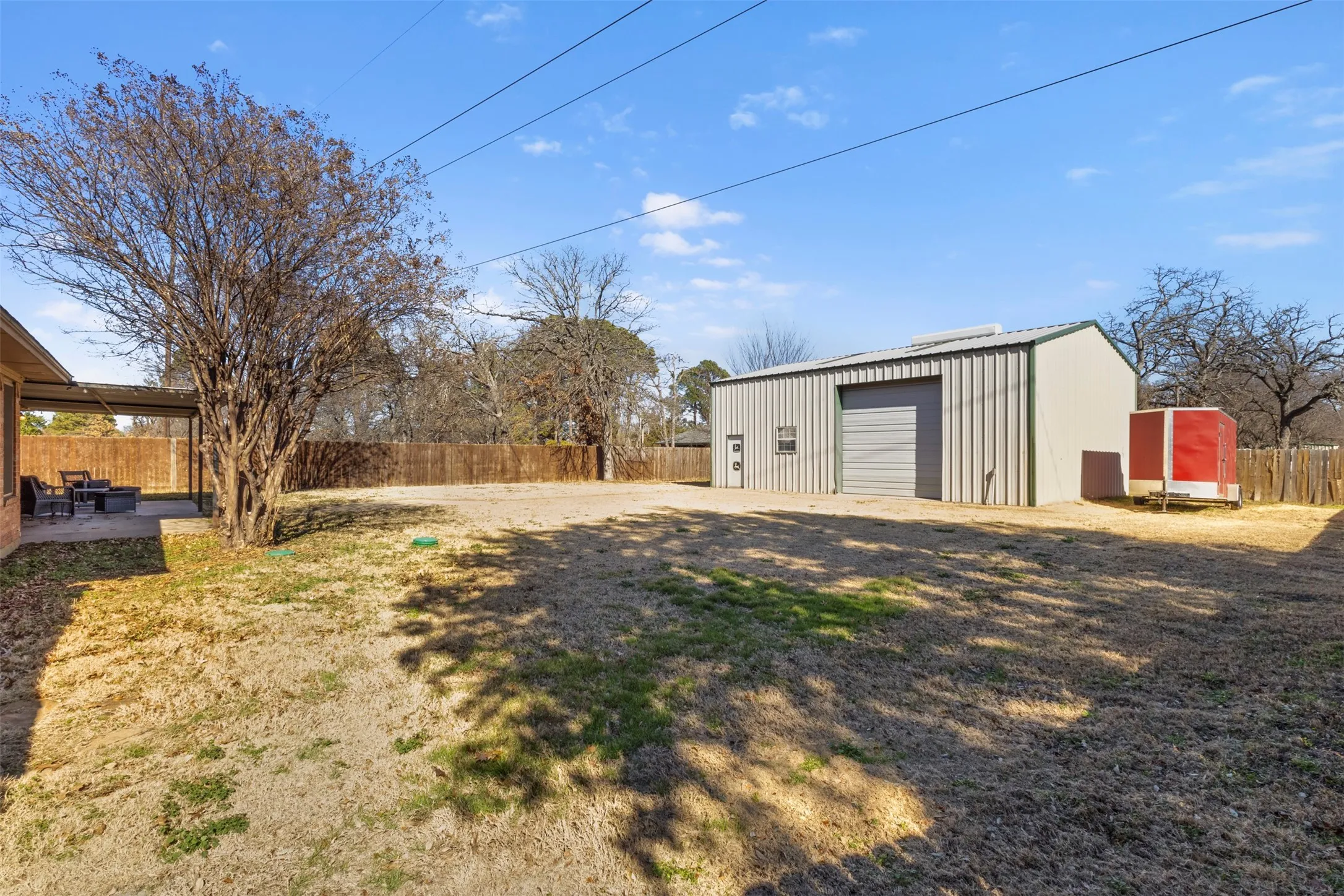Expansive backyard featuring a large metal workshop with a roll-up door, a covered patio, and a wood privacy fence