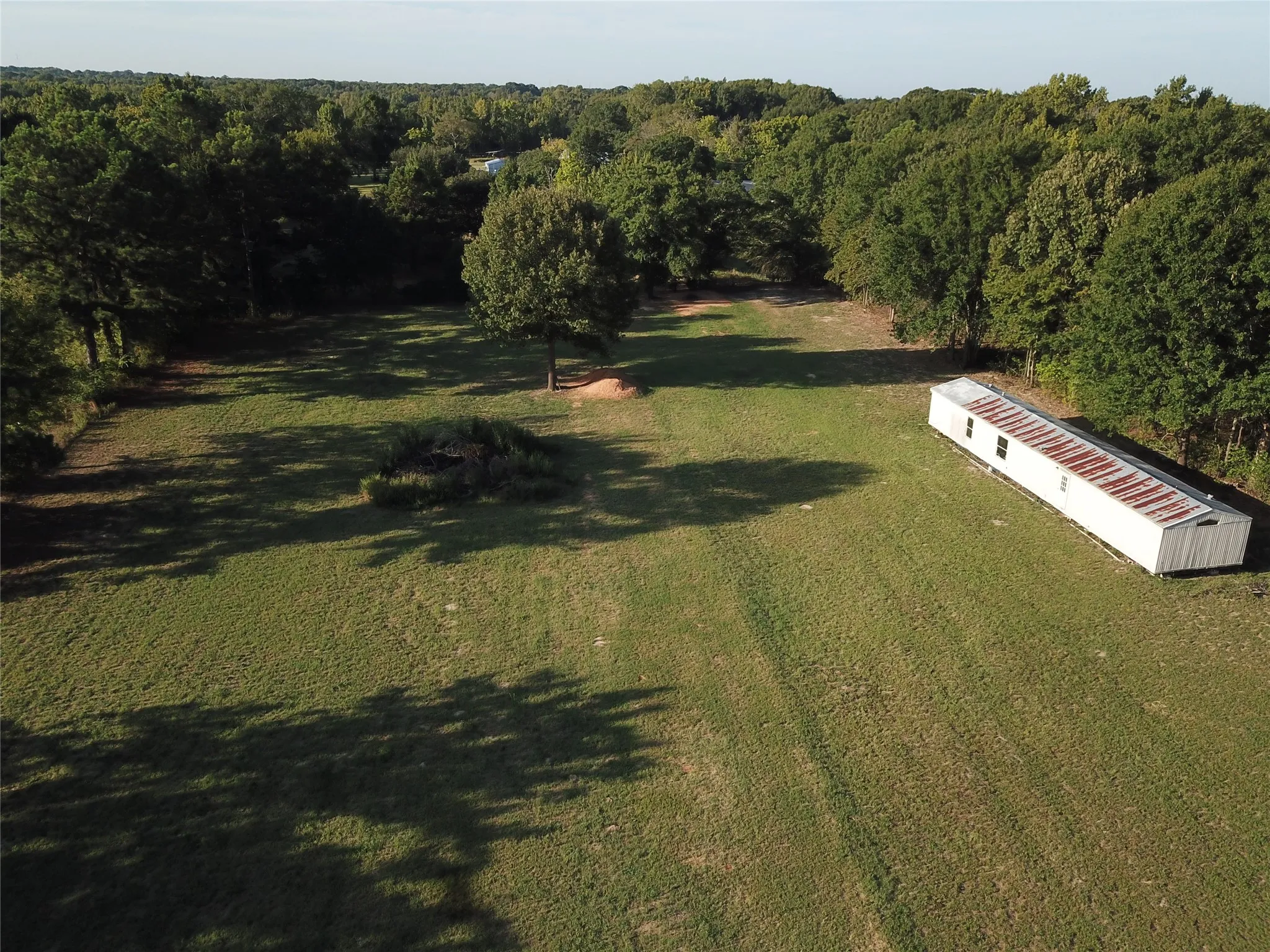 Expansive green space featuring scattered trees and a white mobile structure with a corrugated roof