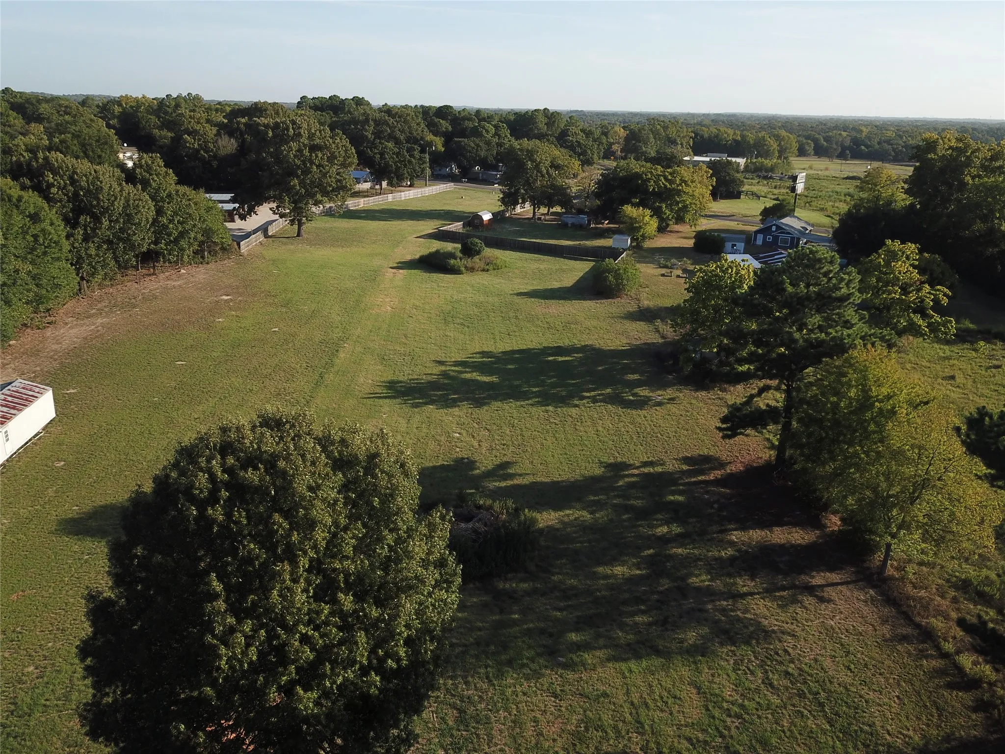 Expansive green space with scattered mature trees and distant residential structures