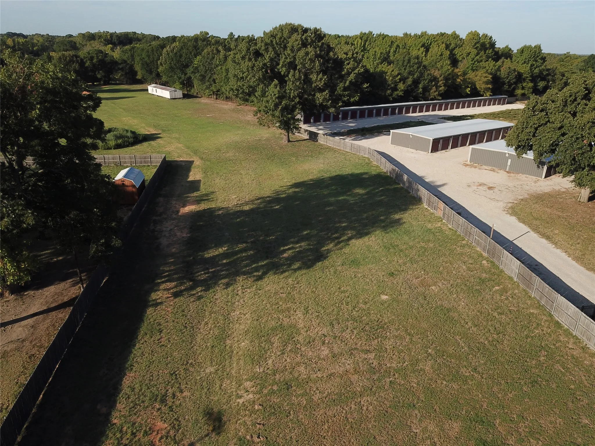 Expansive land parcel featuring open green space, a wood fence perimeter, and mature trees