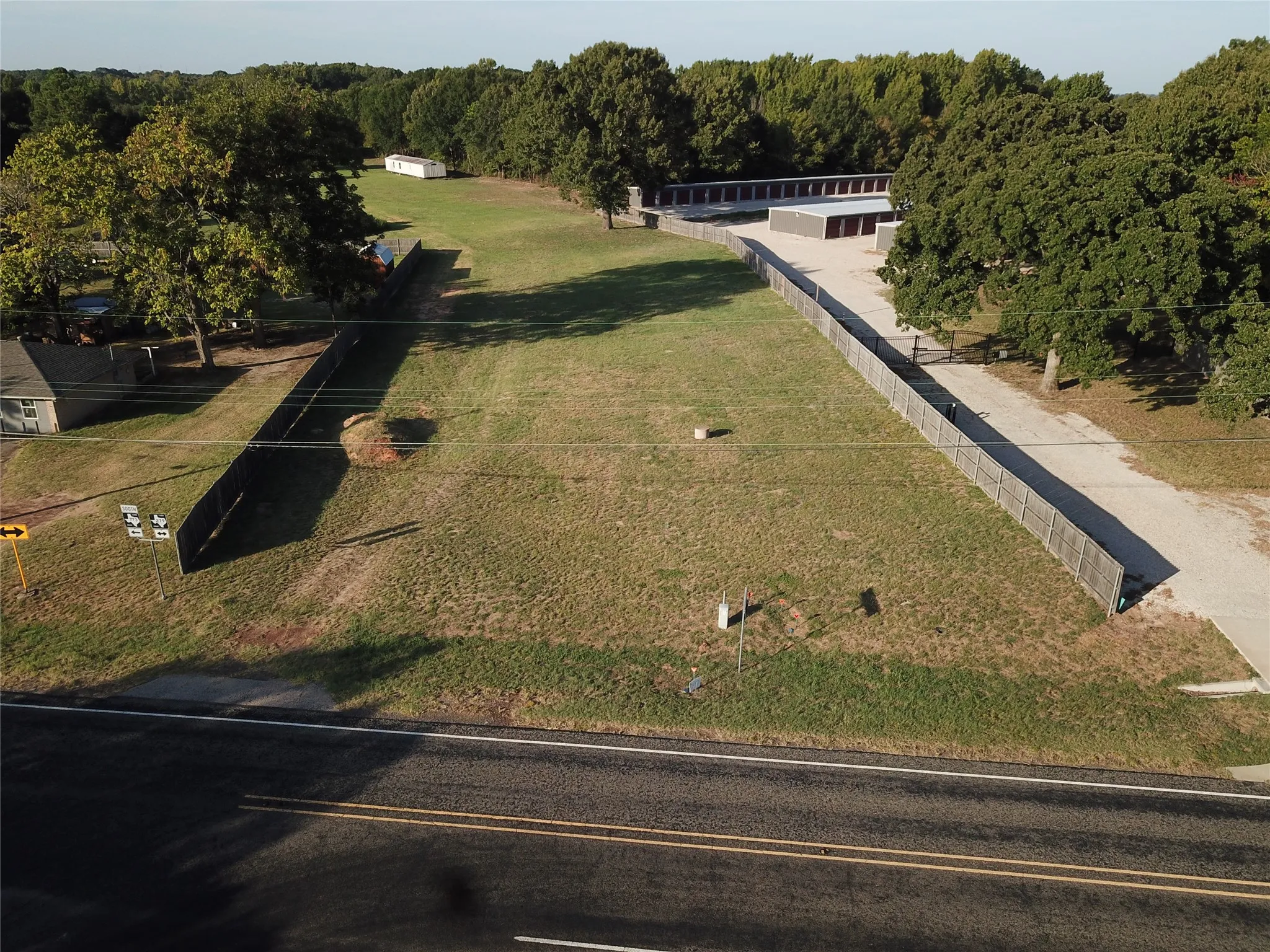Expansive cleared lot with mature perimeter trees, paved road frontage, and privacy fencing
