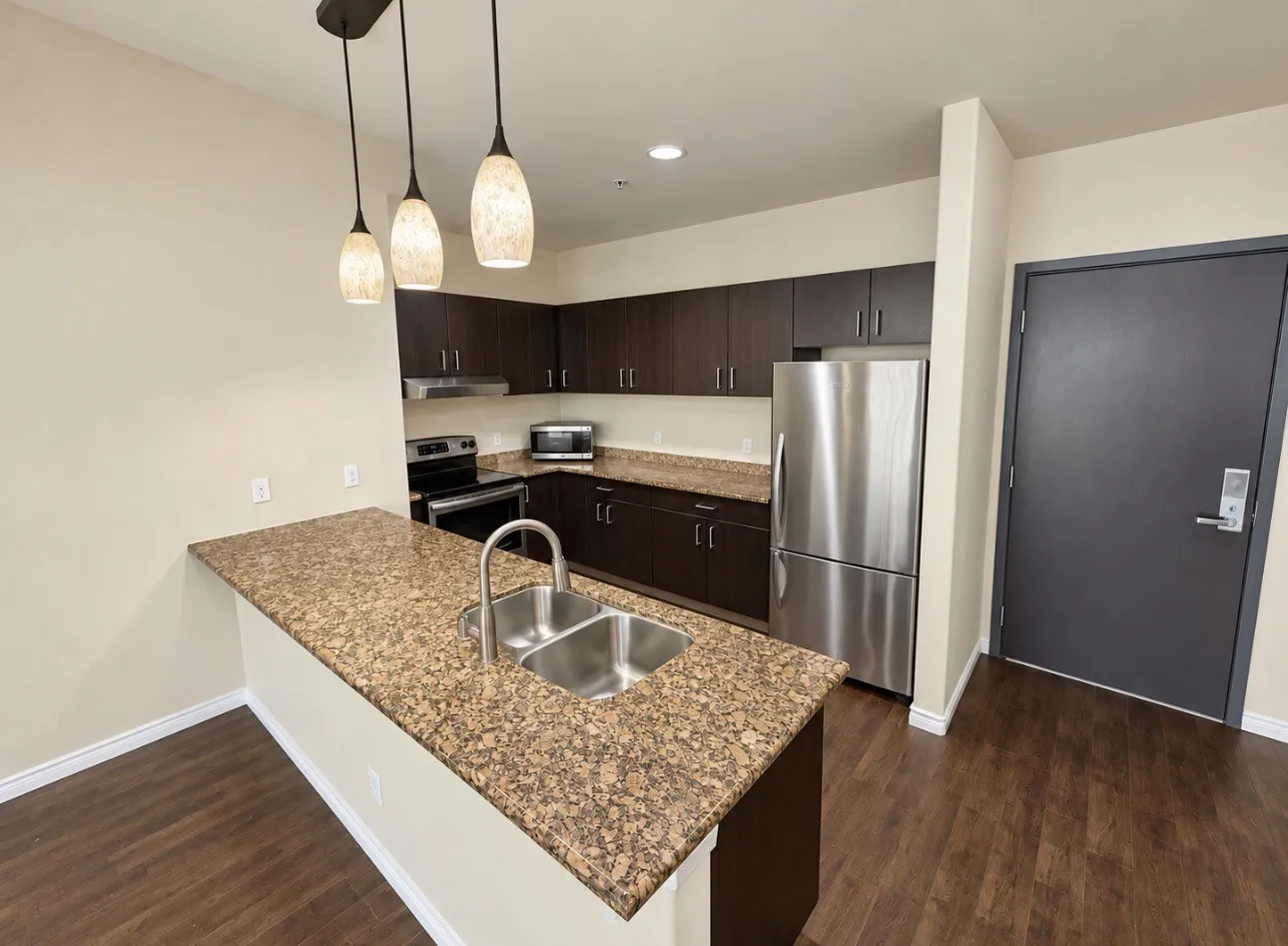 Kitchen featuring dark wood-finish cabinetry, stainless steel appliances, speckled stone countertops, and wood-finish flooring