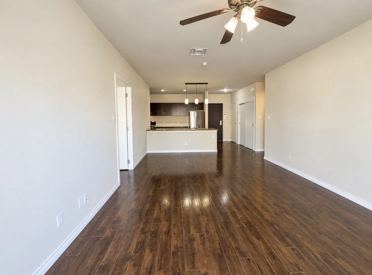 Wood-finish flooring, ceiling fan with integrated lighting, kitchen featuring dark wood cabinetry, stainless steel appliances, and pendant lighting