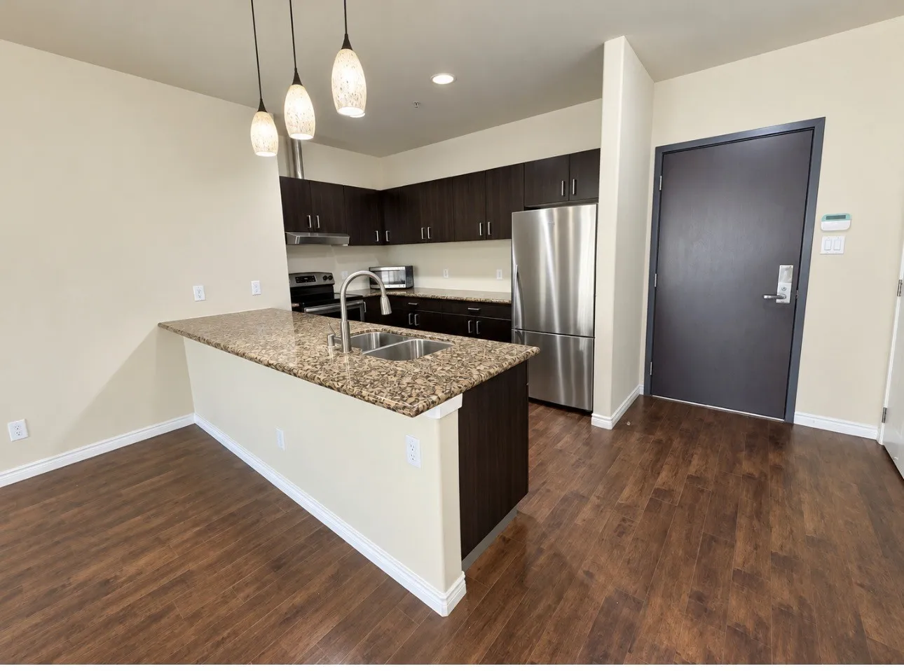 Kitchen featuring a peninsula with granite countertops, stainless steel double-basin sink, dark wood-finish cabinetry, and stainless steel appliances
