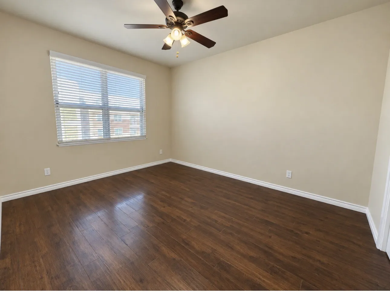 Wood-finish flooring with a neutral wall palette, featuring a window with horizontal blinds and a ceiling fan