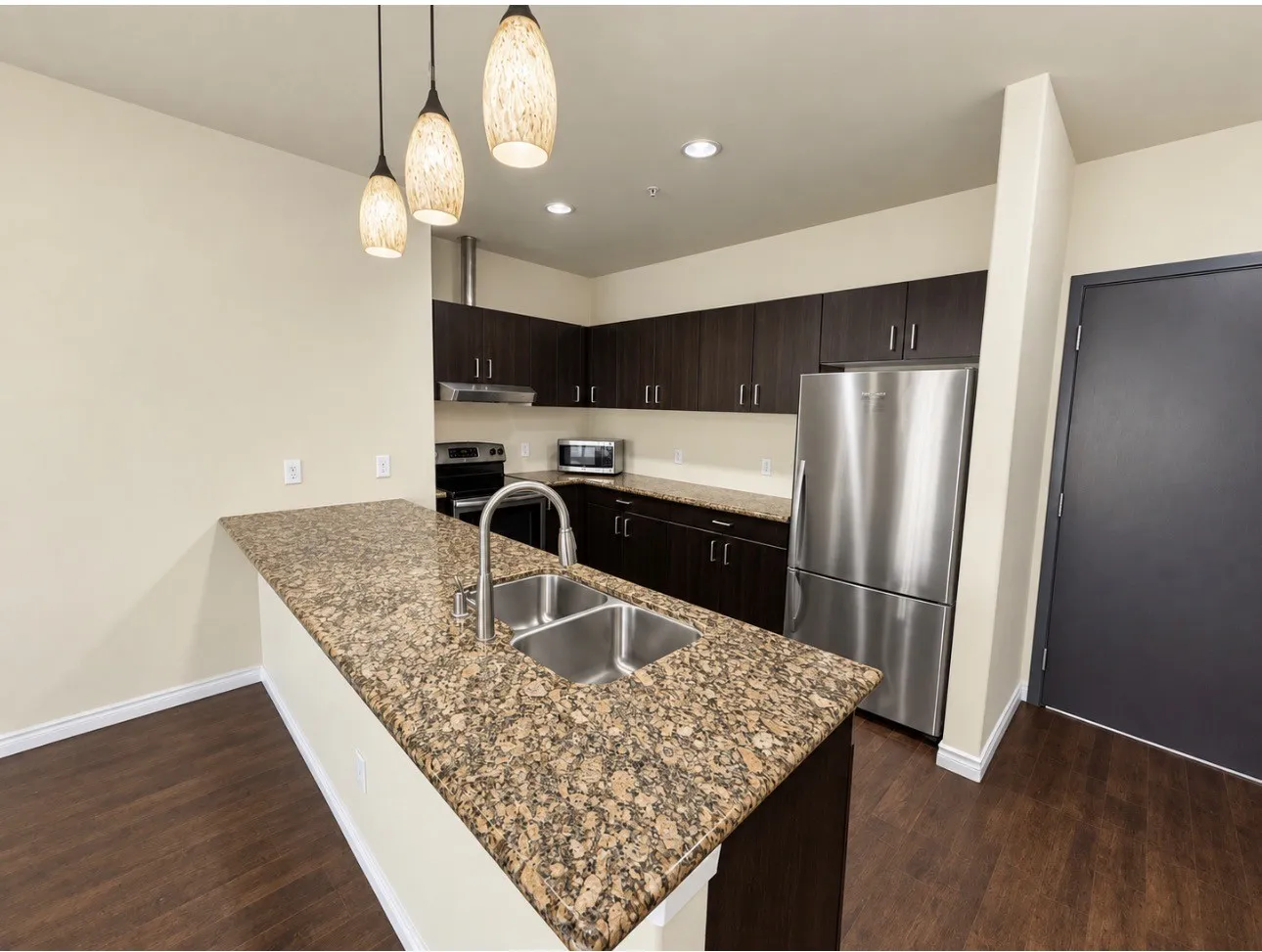 Kitchen featuring dark wood-finish cabinetry, stainless steel appliances, a dual-basin sink, and granite countertops