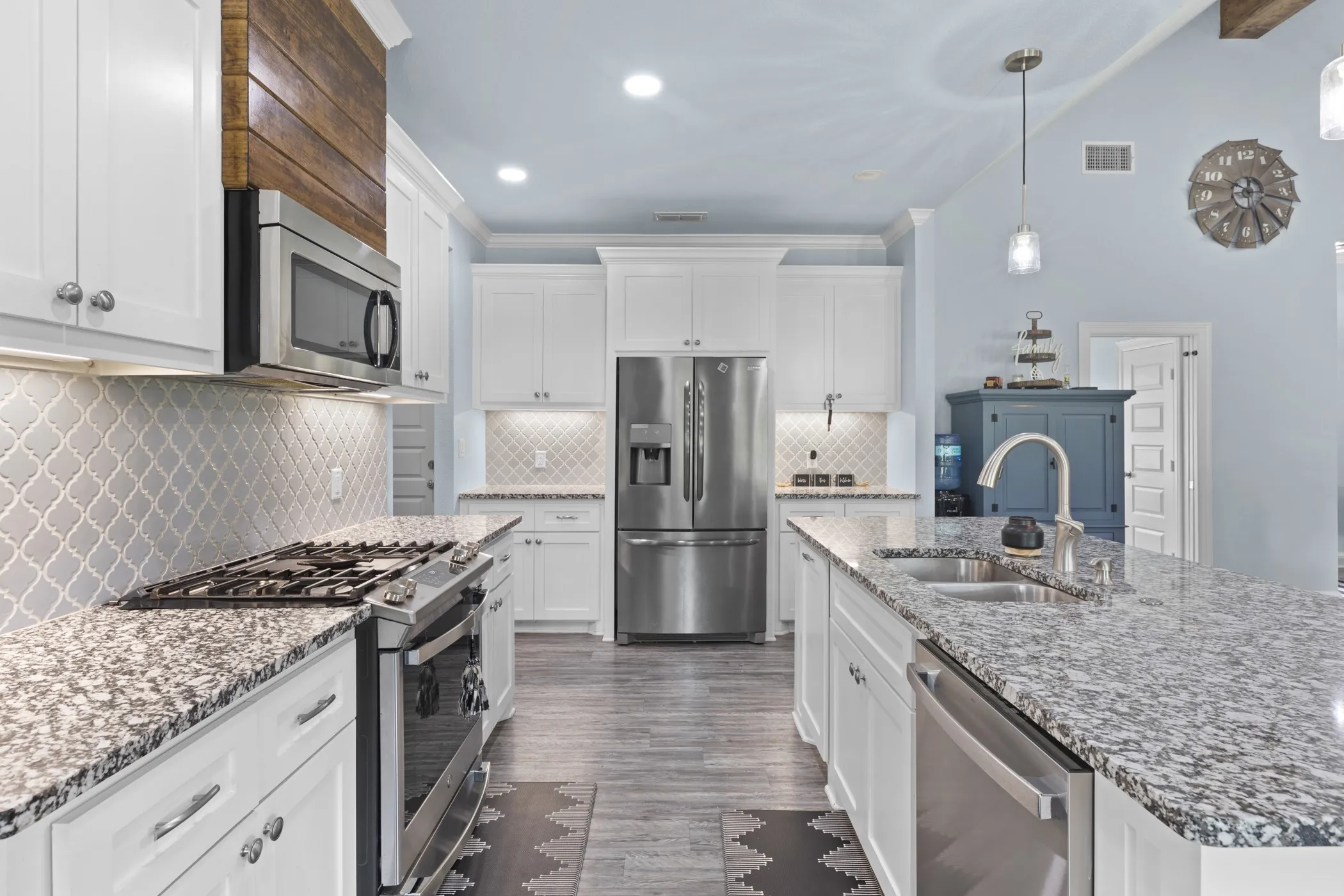 White cabinetry, stainless steel appliances, granite countertops, decorative tile backsplash, and wood-finish flooring