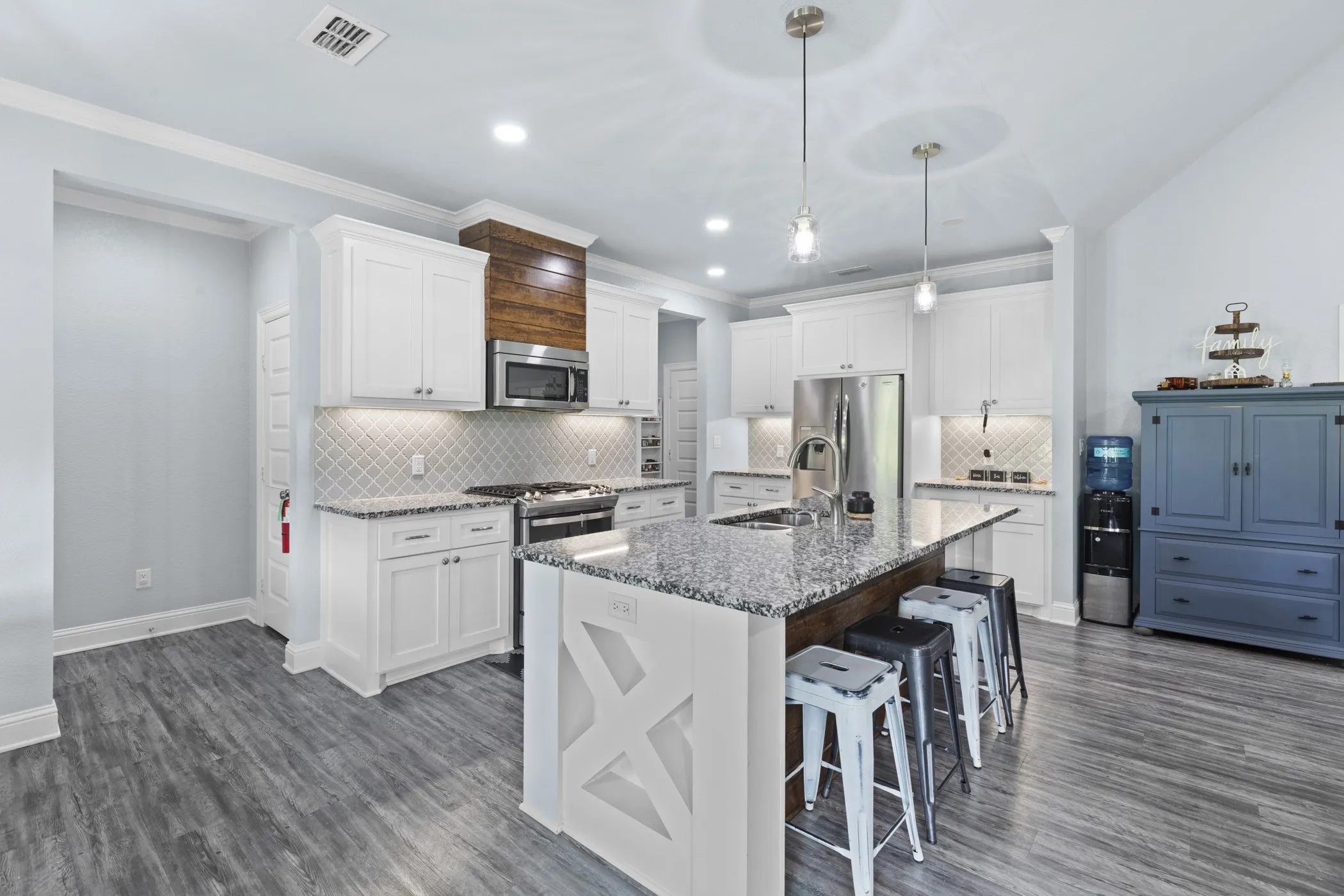 Kitchen featuring white cabinetry, gray wood-finish flooring, a central island with a granite countertop, stainless steel appliances, and pendant lighting