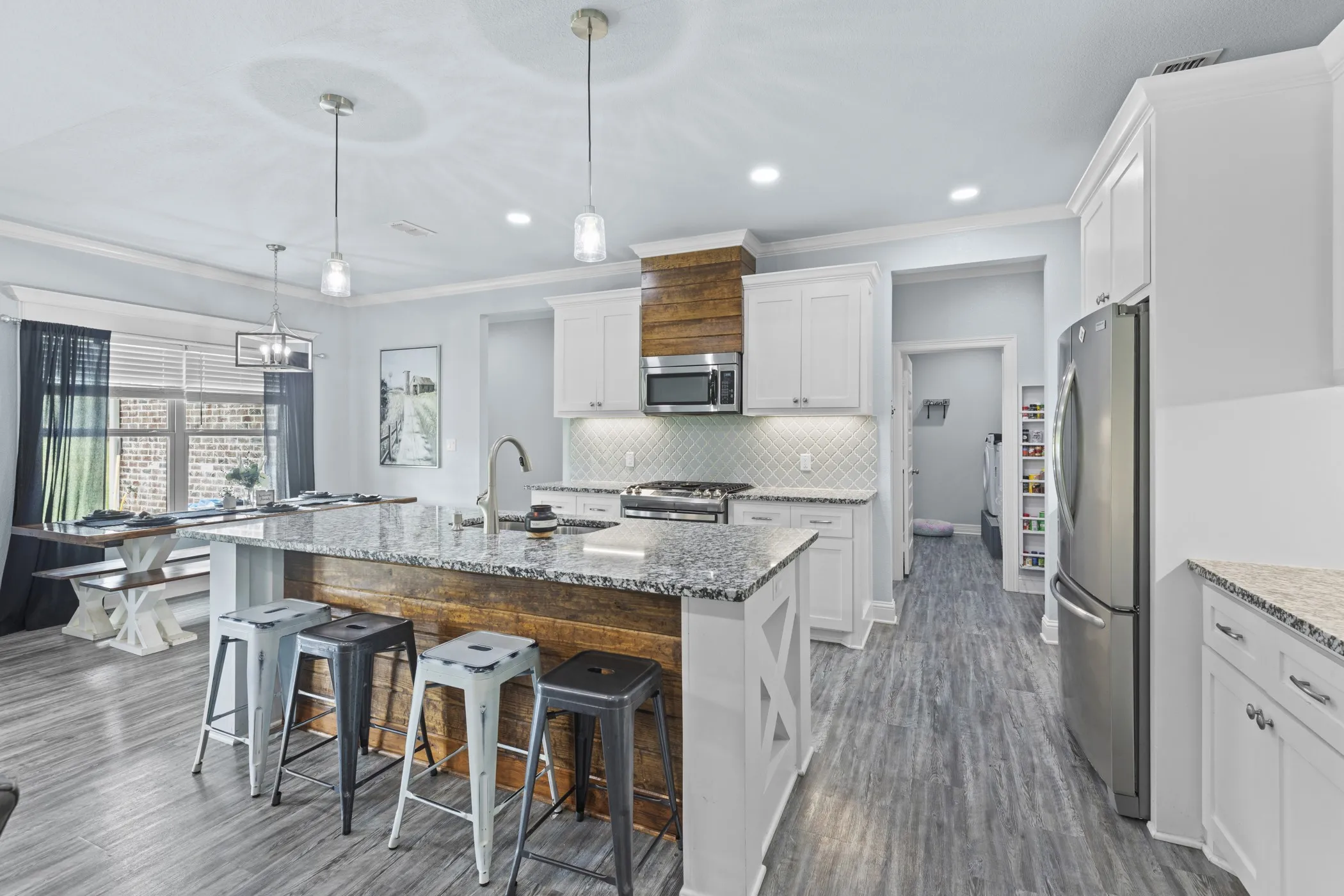 Kitchen featuring a large island with a stone counter, wood-finish flooring, white cabinetry, integrated stainless steel appliances, and a tiled backsplash