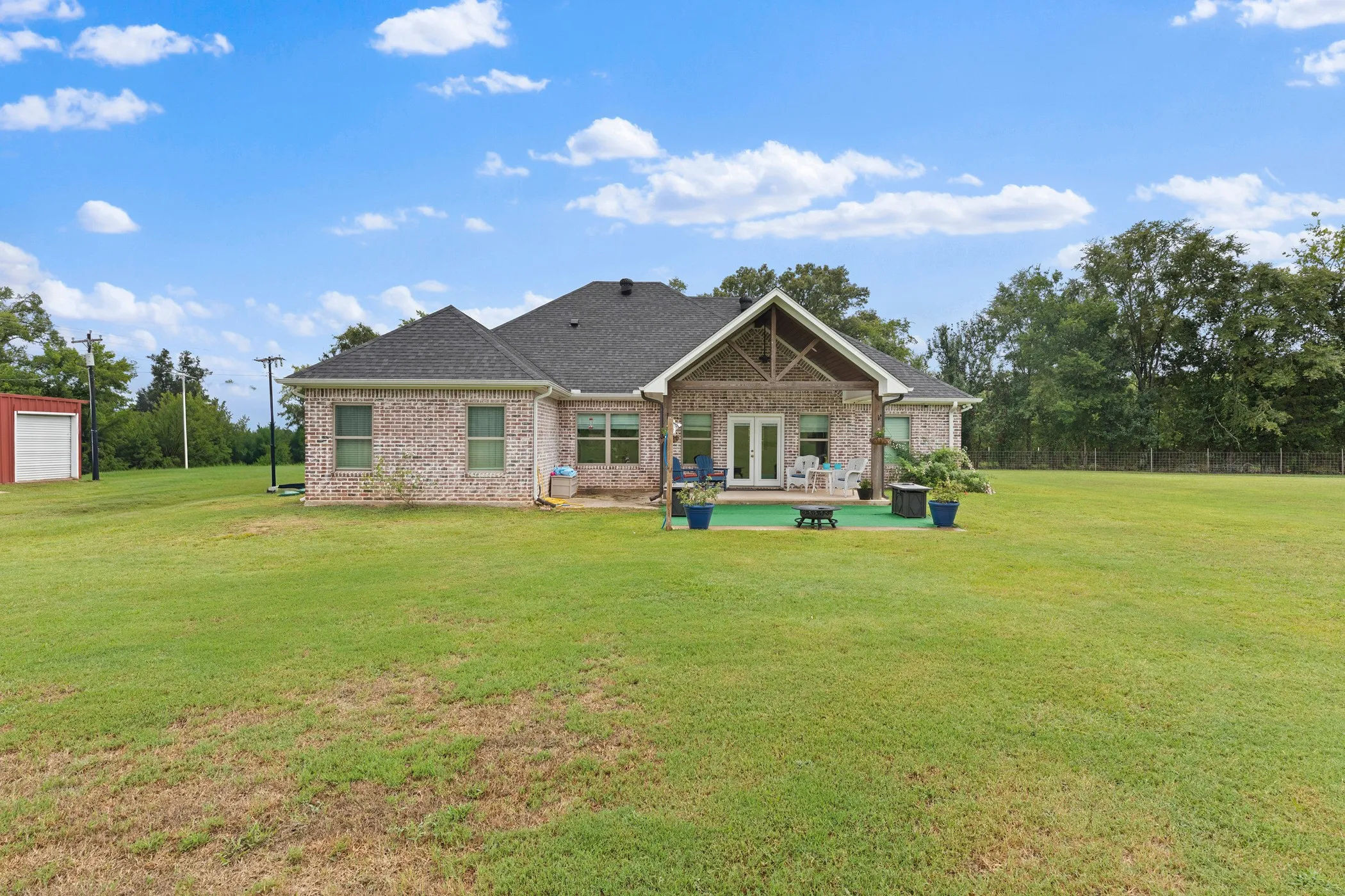 Expansive green lawn with a brick exterior, covered patio, double glass doors, and a detached storage building