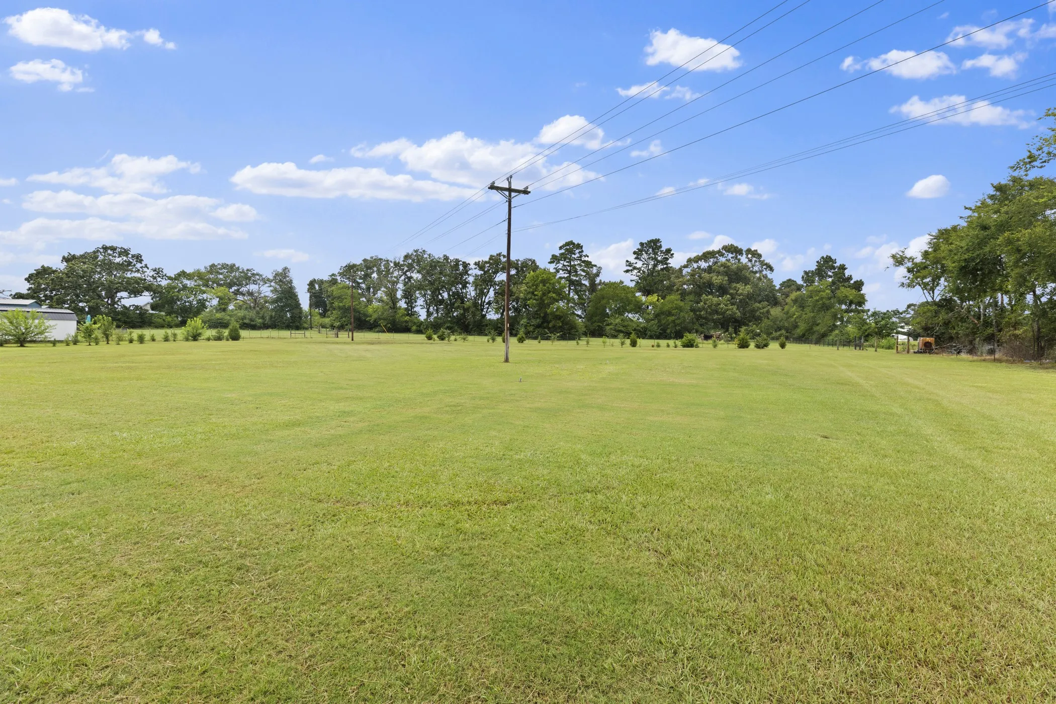 Expansive grass field with partial fencing and distant trees
