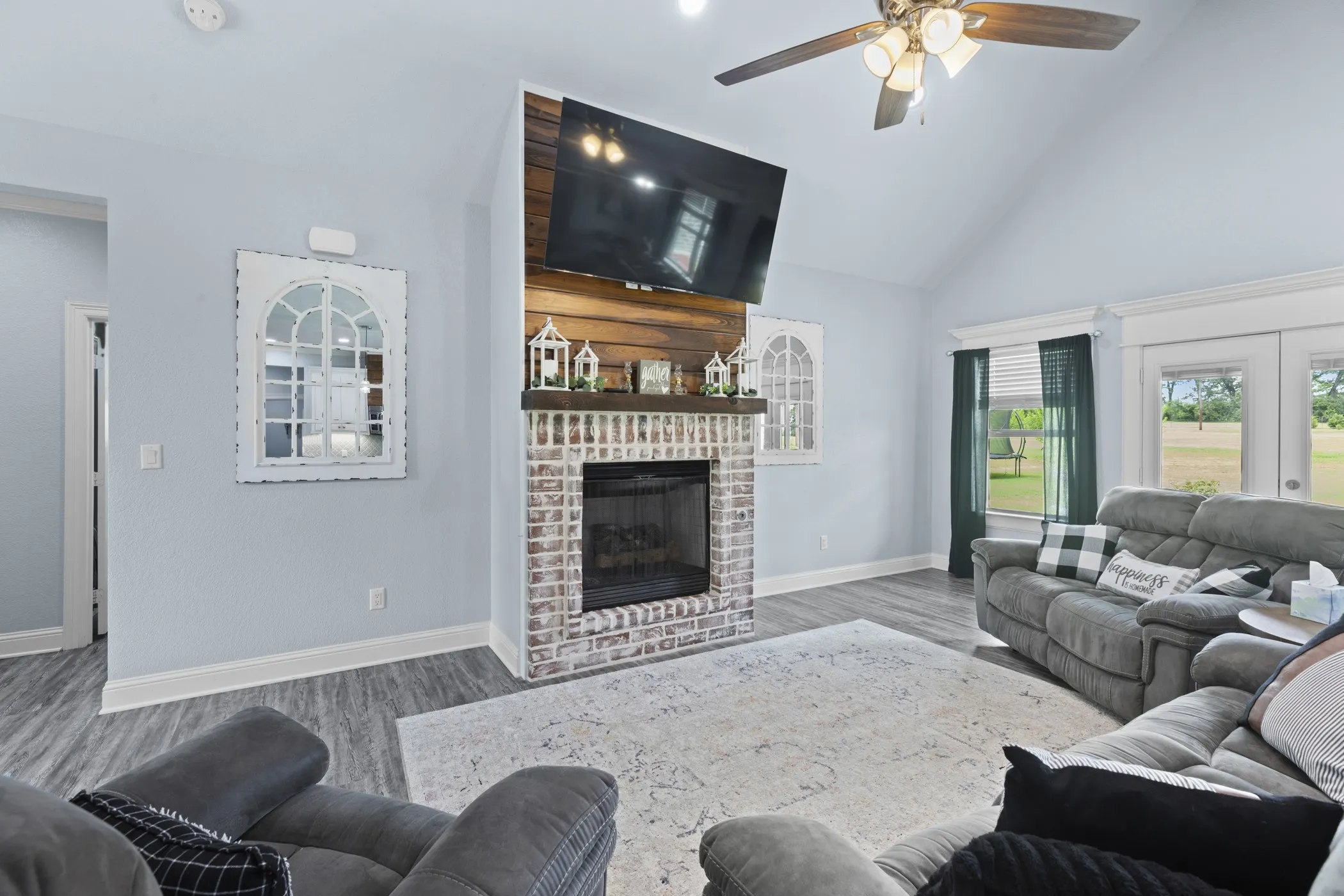 Vaulted ceiling, wood-finish flooring, brick fireplace with wood mantel, built-in ceiling fan, and French doors