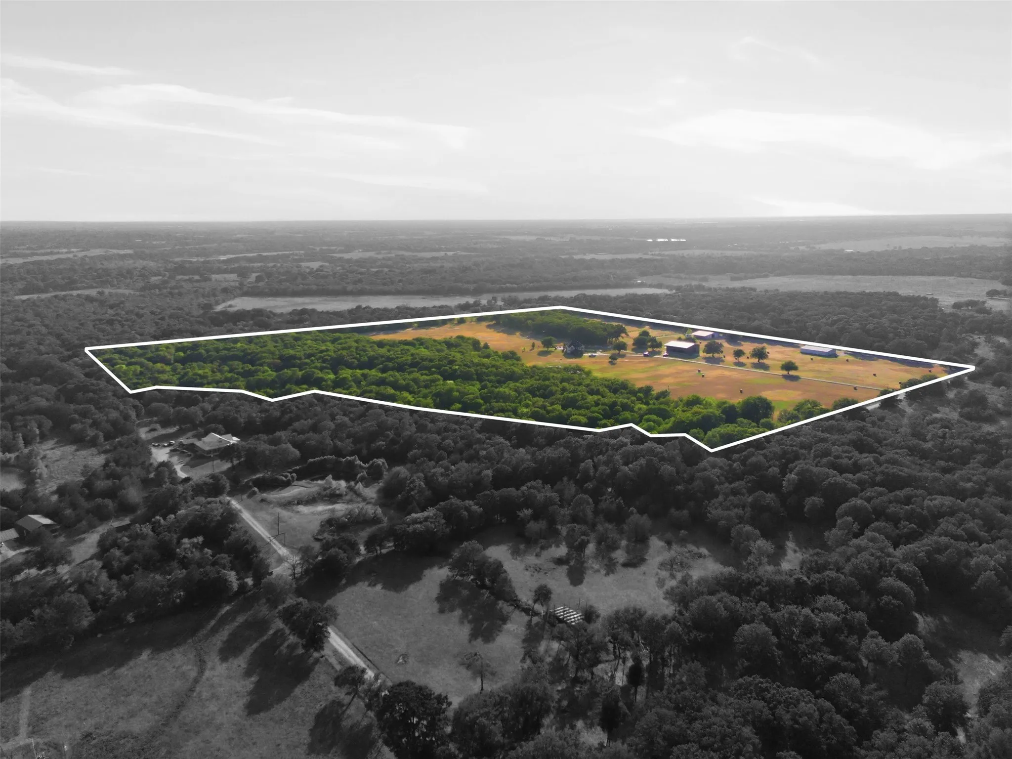 Expansive property featuring mature trees, open fields, multiple outbuildings, and a main residence