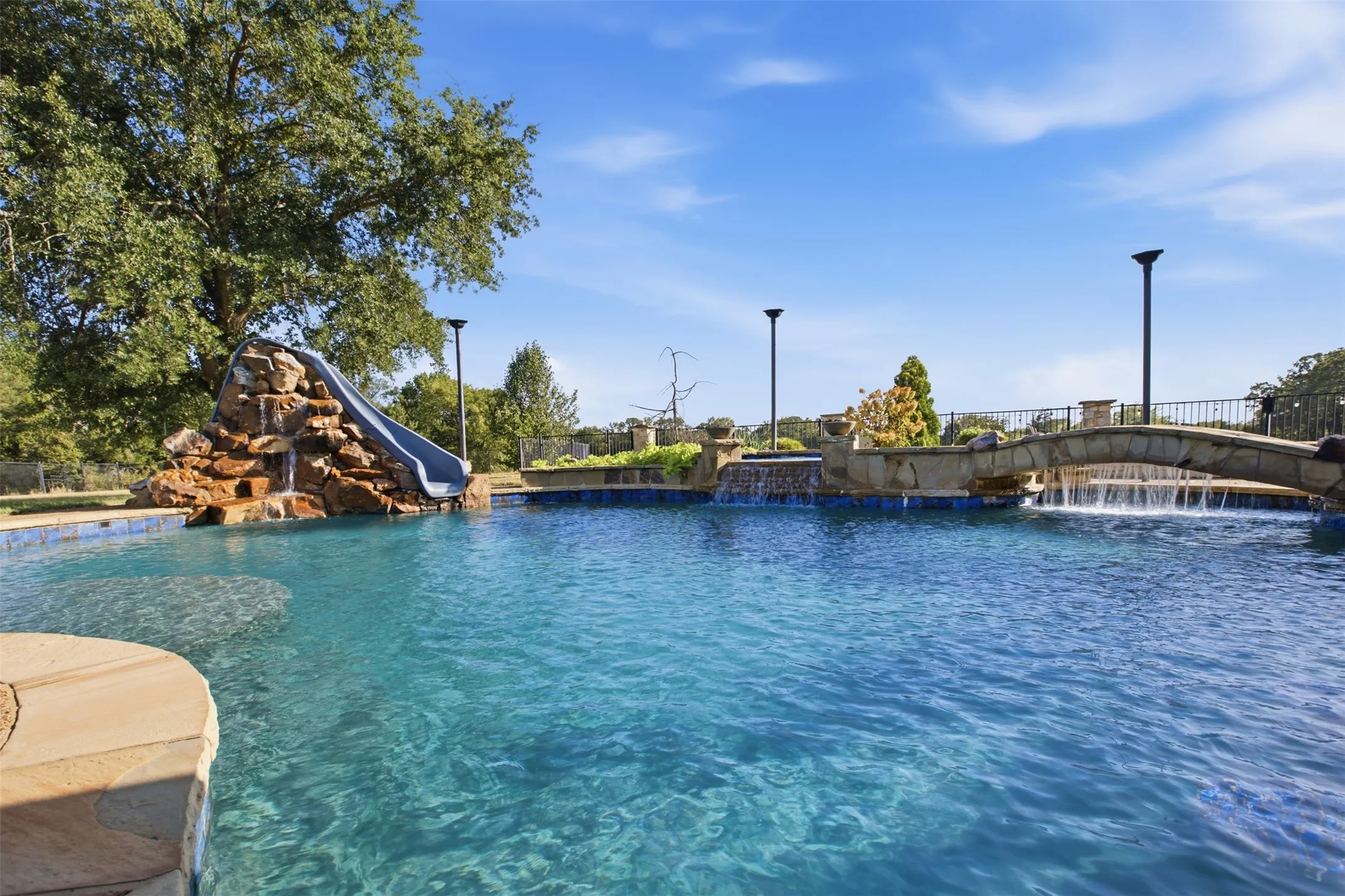 Swimming pool featuring a rock waterfall, built-in slide, stone bridge, and integrated water features