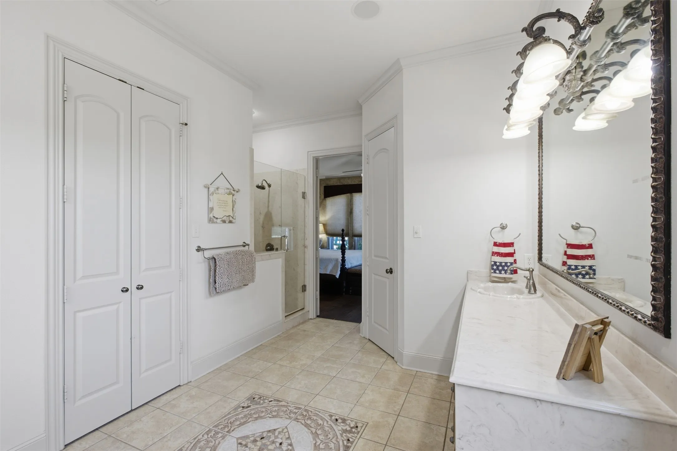 White paneled doors, tile flooring, glass-enclosed shower, built-in vanity with integrated sink, and an ornate mirror with sconce lighting