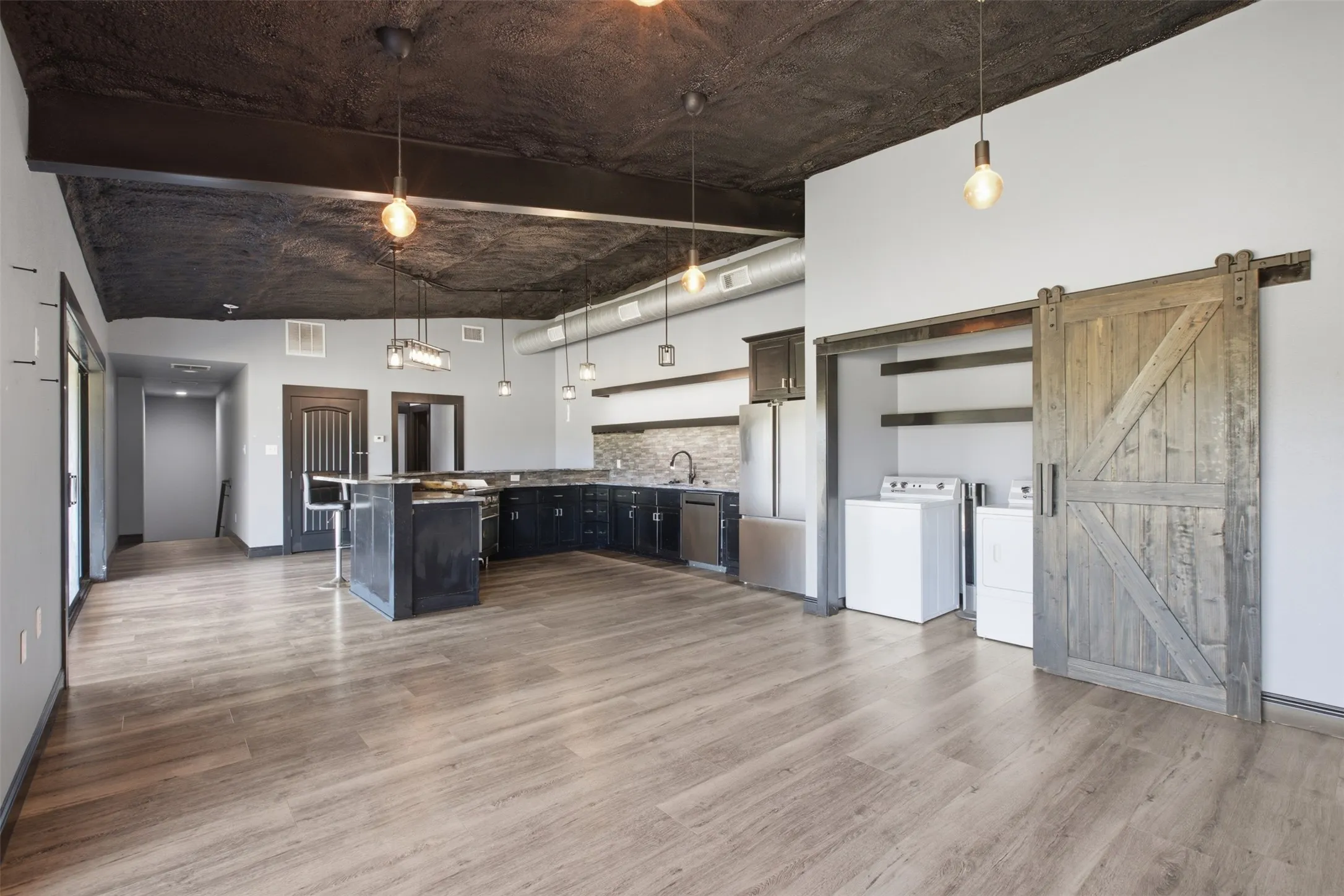 Open-concept living area with wood-finish flooring, a kitchen island, dark cabinetry, and stainless steel appliances