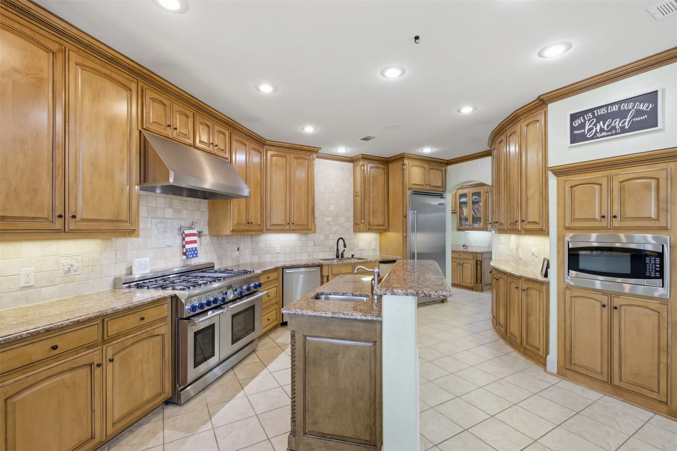 Extensive cabinetry with decorative crown molding, stainless steel appliances, granite countertops, tile flooring, and recessed lighting
