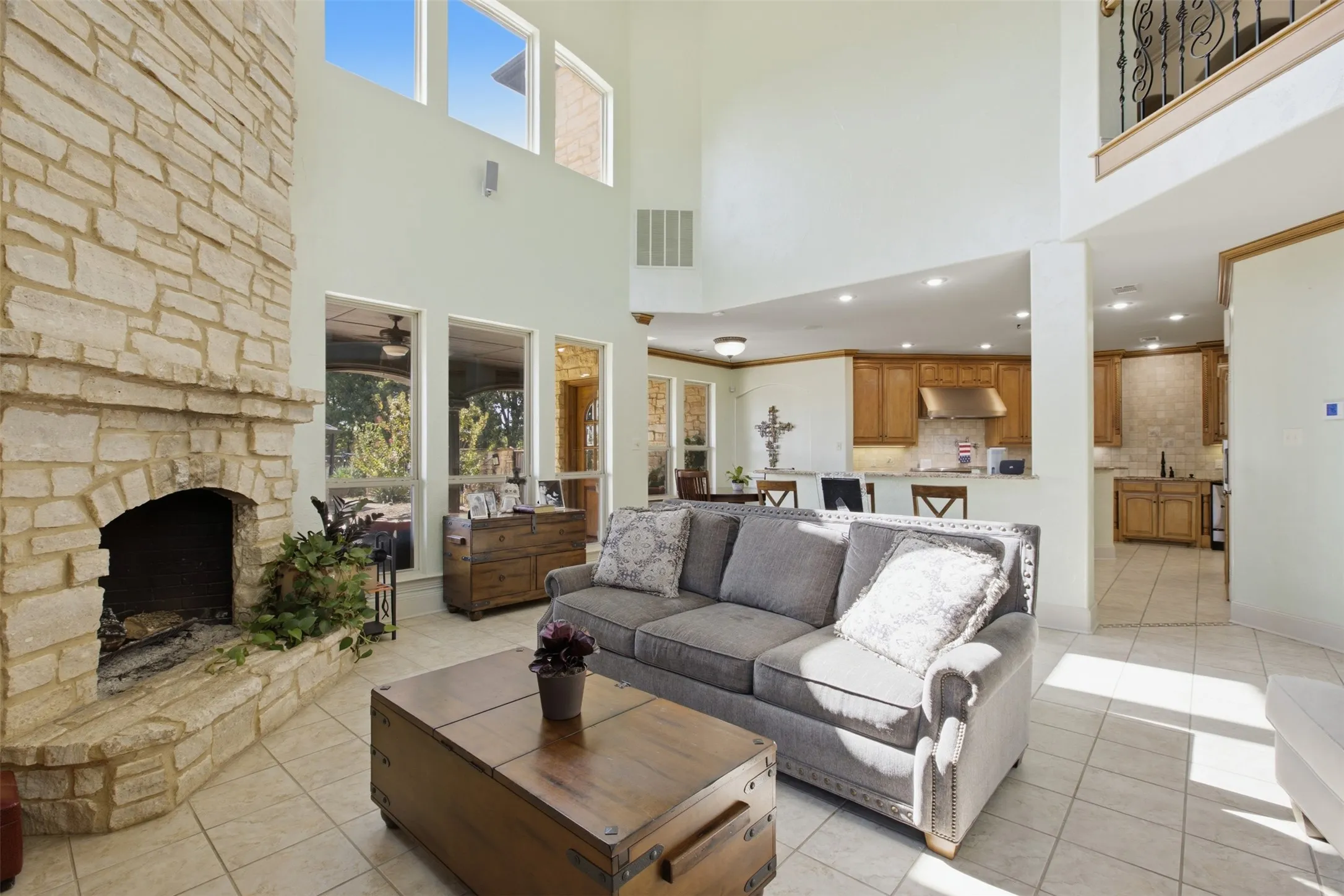 Two-story living area with a stone fireplace, ceramic tile flooring, and multiple large windows