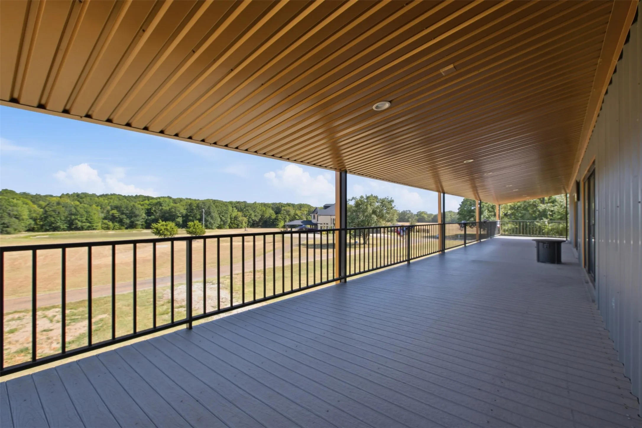 Expansive covered patio with a gray deck surface, black metal railing, and a wood-finish ceiling
