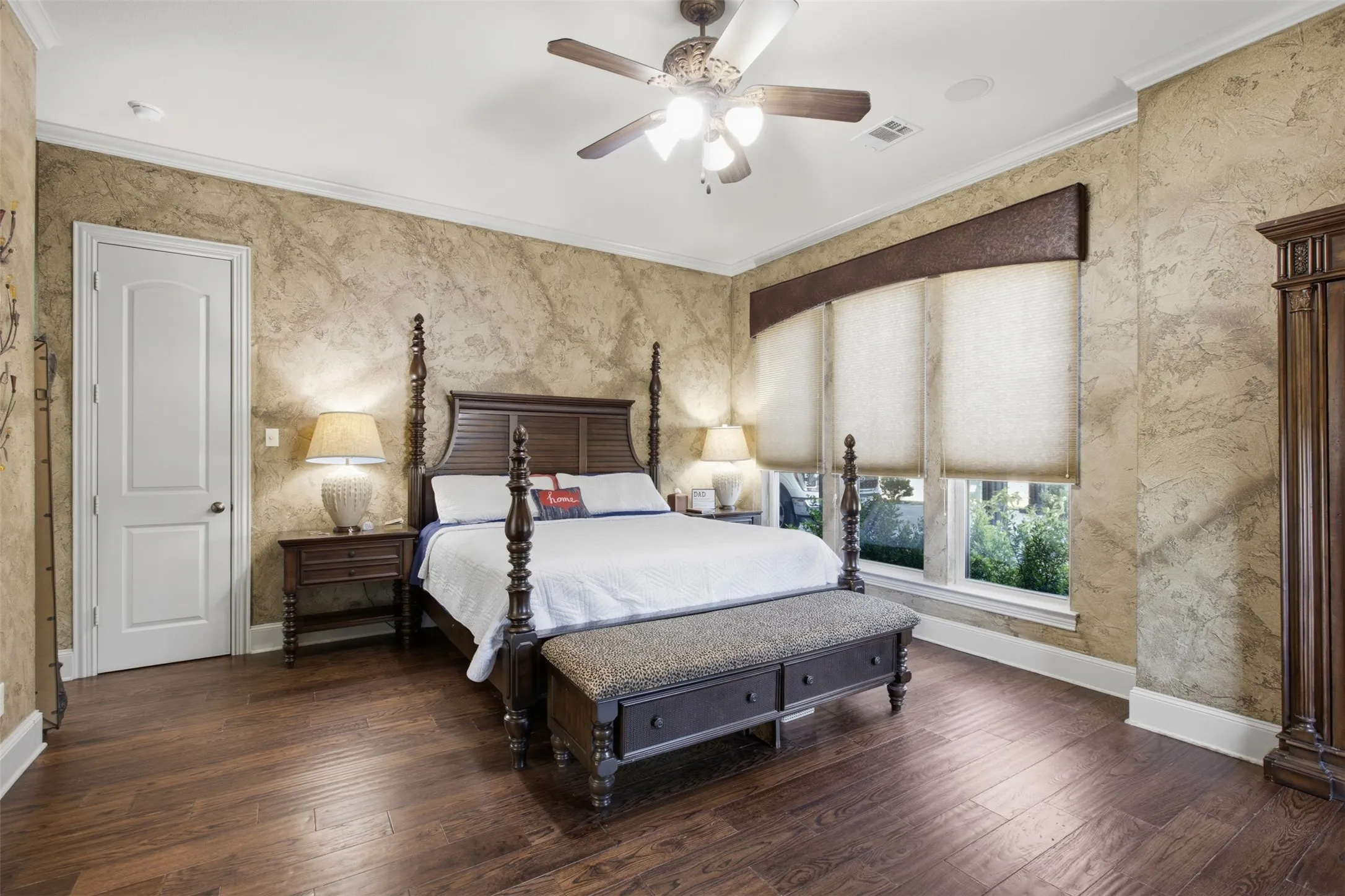 Wood-finish flooring throughout, featuring a ceiling fan, crown molding, and multiple windows with custom window treatments