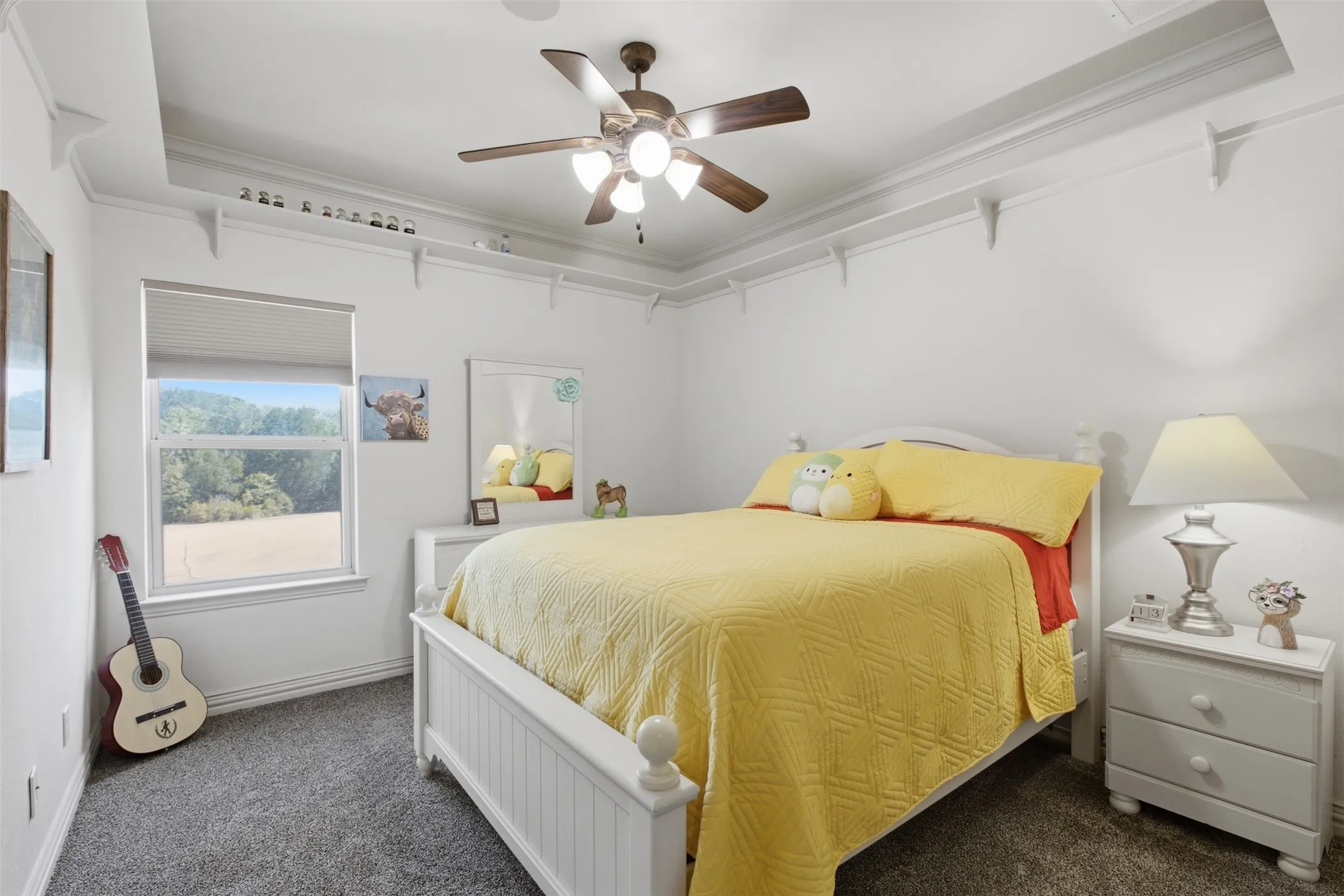 Recessed ceiling with layered crown molding, ceiling fan with integrated lighting, carpeted flooring, and a window with roller shade