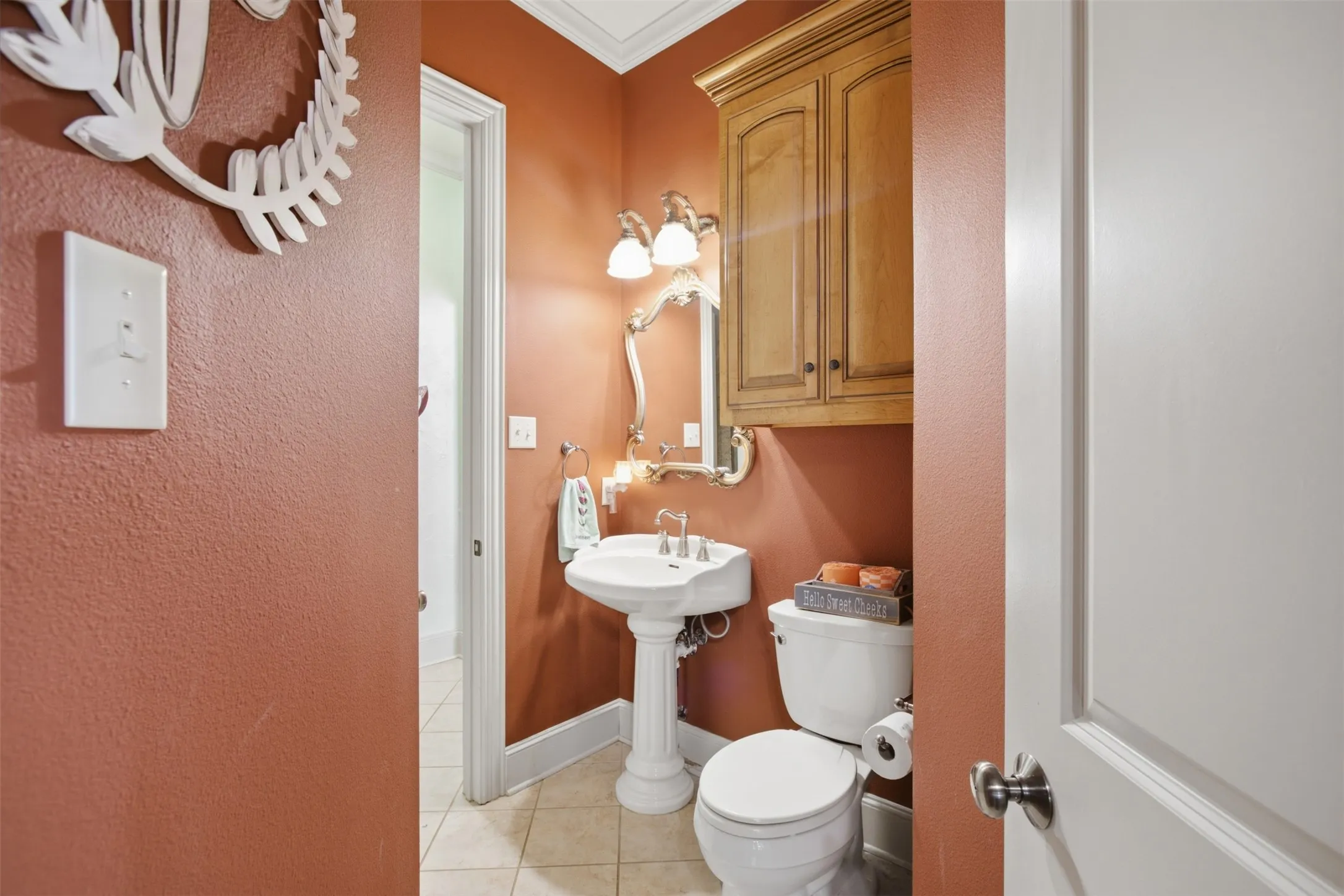 Pedestal sink with dual faucet, wall-mounted light fixture, and wood-finish cabinetry