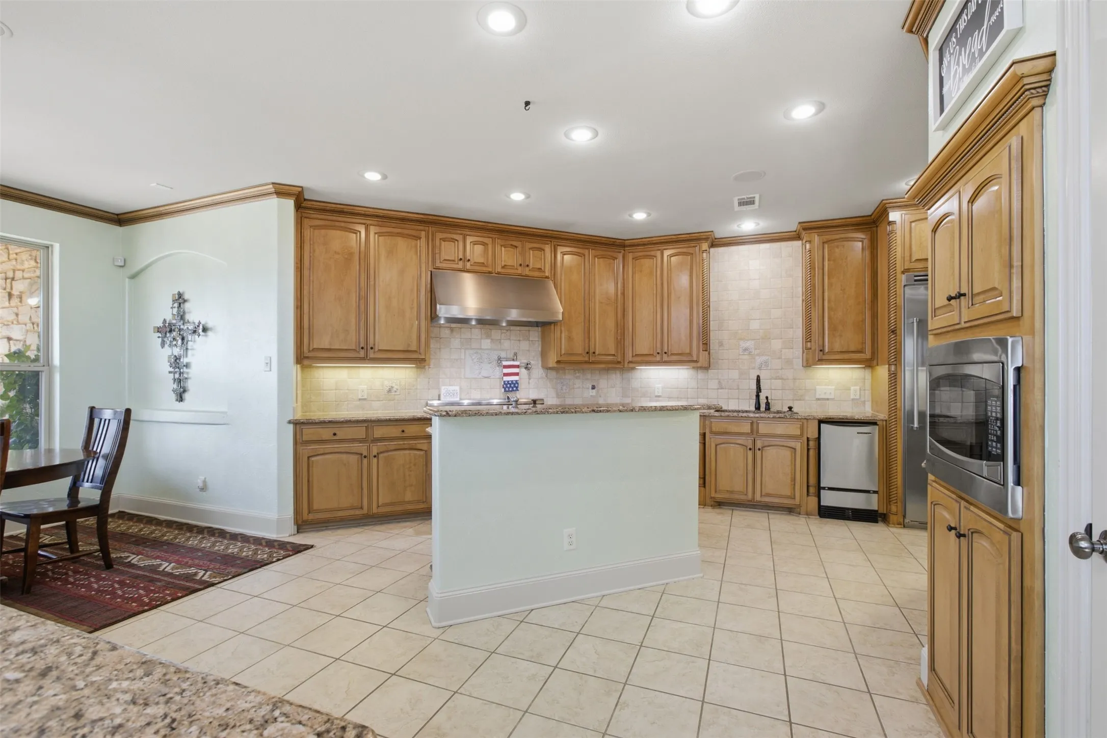 Kitchen featuring warm wood cabinetry, neutral tile flooring, granite countertops, and stainless steel appliances