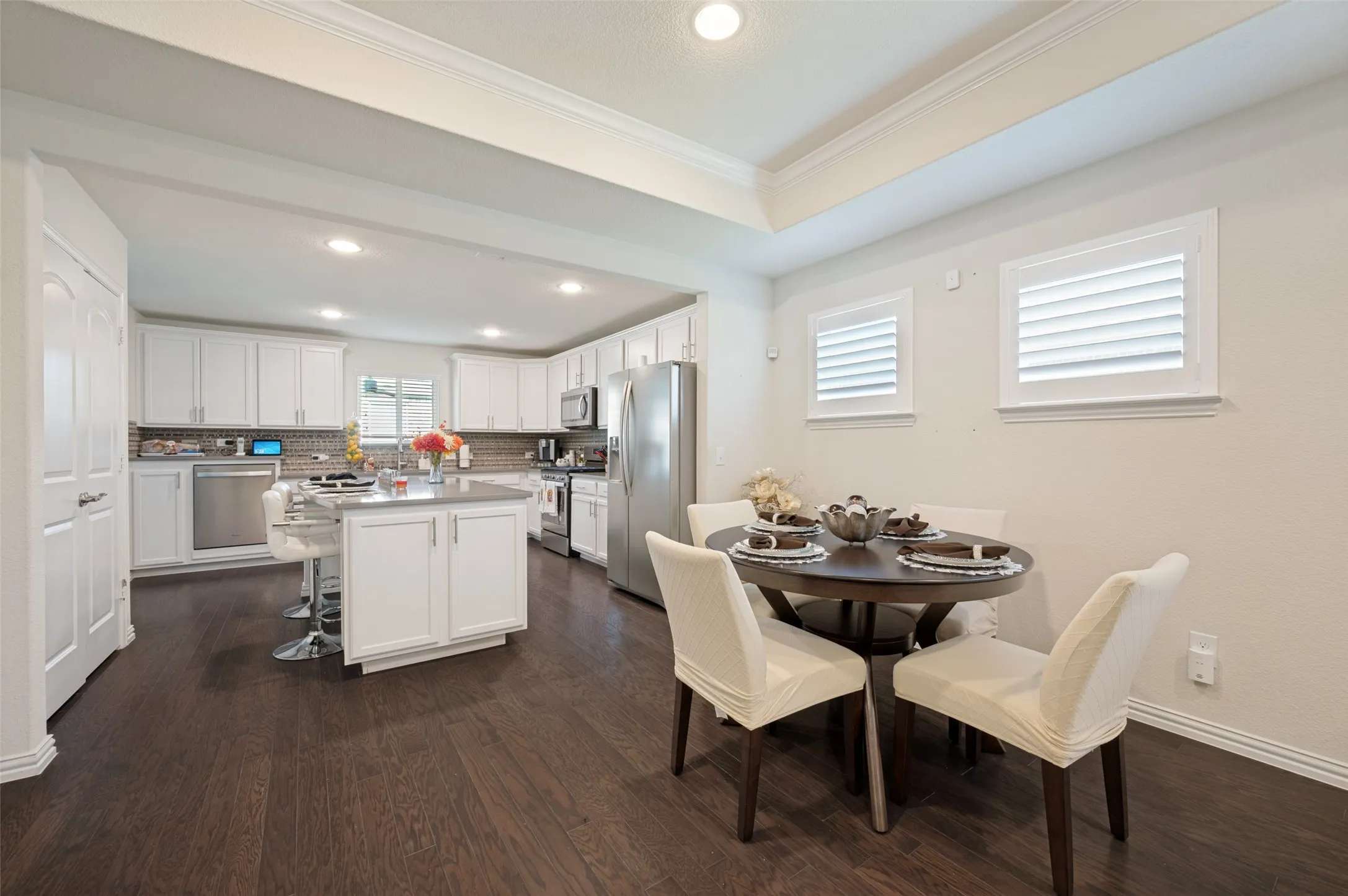 Kitchen and dining area featuring dark wood-finish flooring, white cabinetry, stainless steel appliances, and a central island with counter seating
