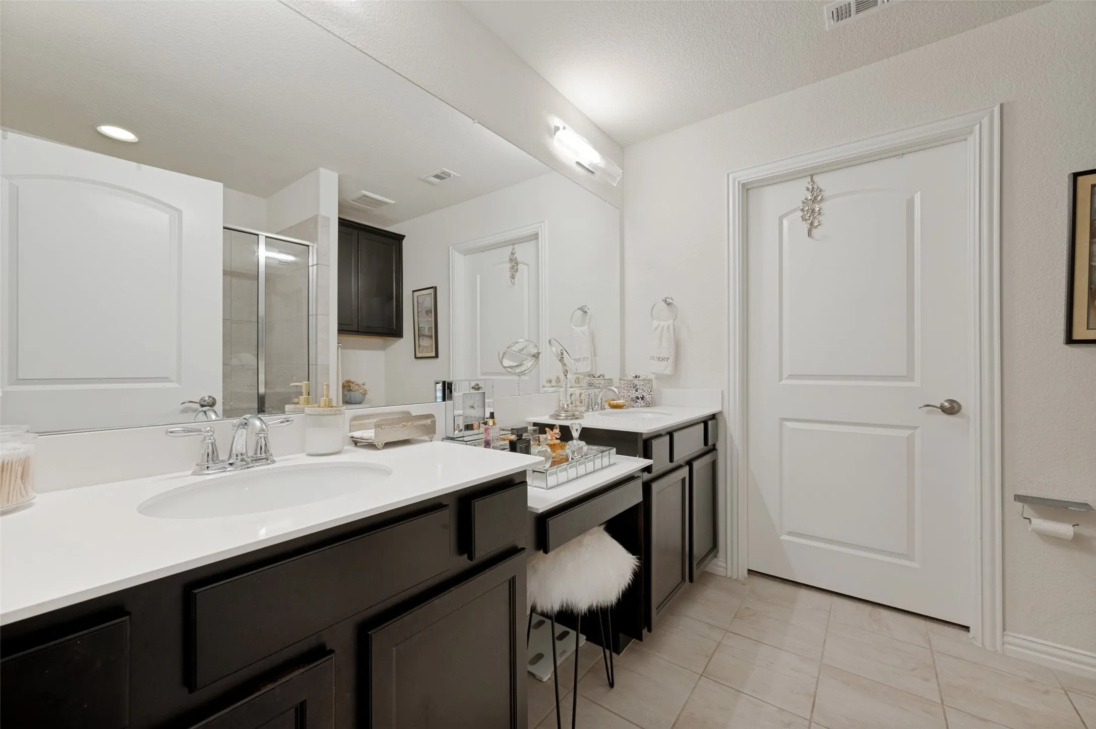 Dual undermount sinks with chrome fixtures, an expansive counter, dark wood cabinetry, and a mirrored vanity area
